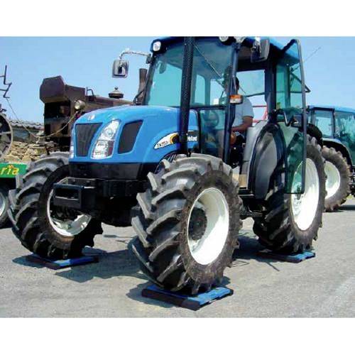 Ein blauer Traktor mit großen Reifen steht auf einer asphaltierten Fläche. Ein ähnliches Fahrzeug ist im Hintergrund erkennbar.