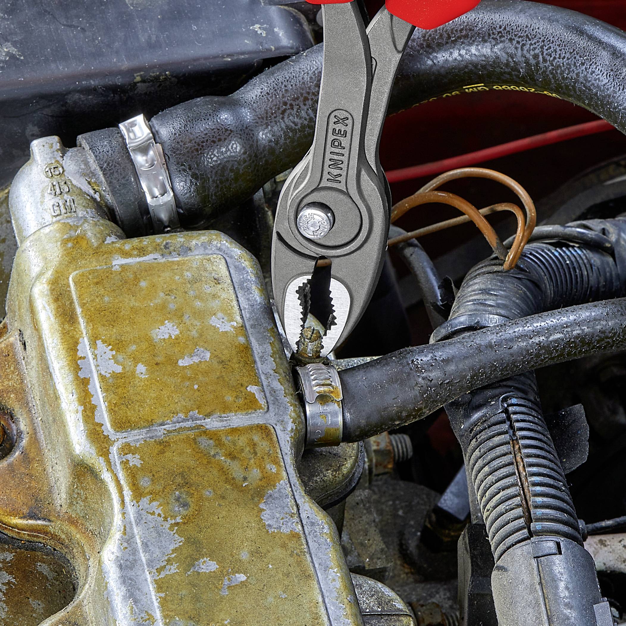 Eine Zange hält ein verrostetes Teil an einem alten Fahrzeugmotor, das die Reparatur oder Wartung demonstriert.