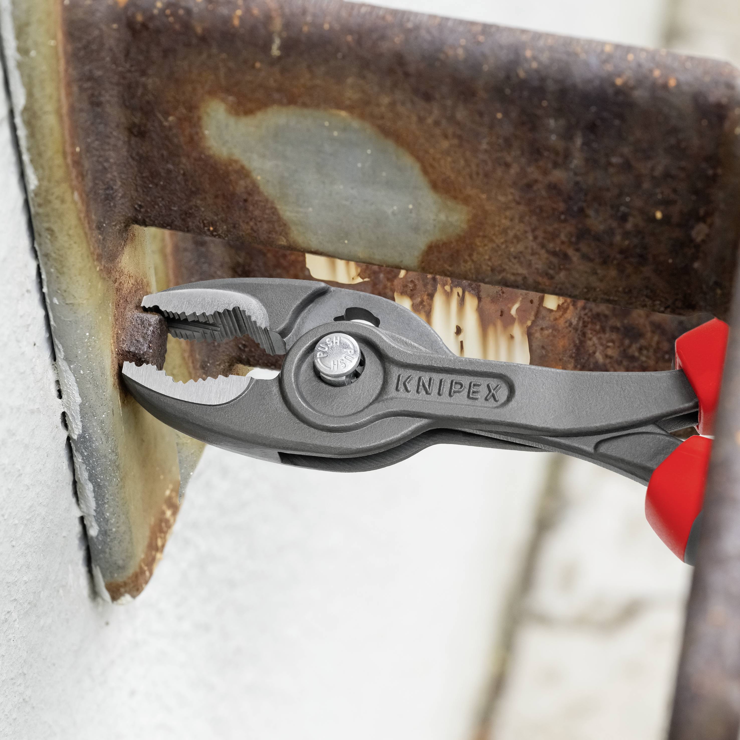 Eine Zange der Marke 'Knipex' hält ein rostiges Stahlteil fest. Die rote Zange ist zum Schraubenlösen an schwierigen Stellen geeignet.
