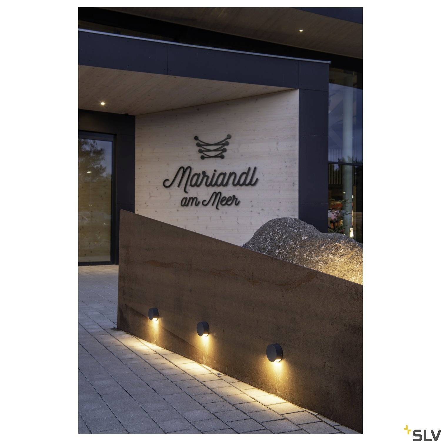 Außenansicht eines Gebäudes mit dem Namen 'Mariandl am Meer' an der Wand. Moderne Außenbeleuchtung entlang einer Steinmauer.