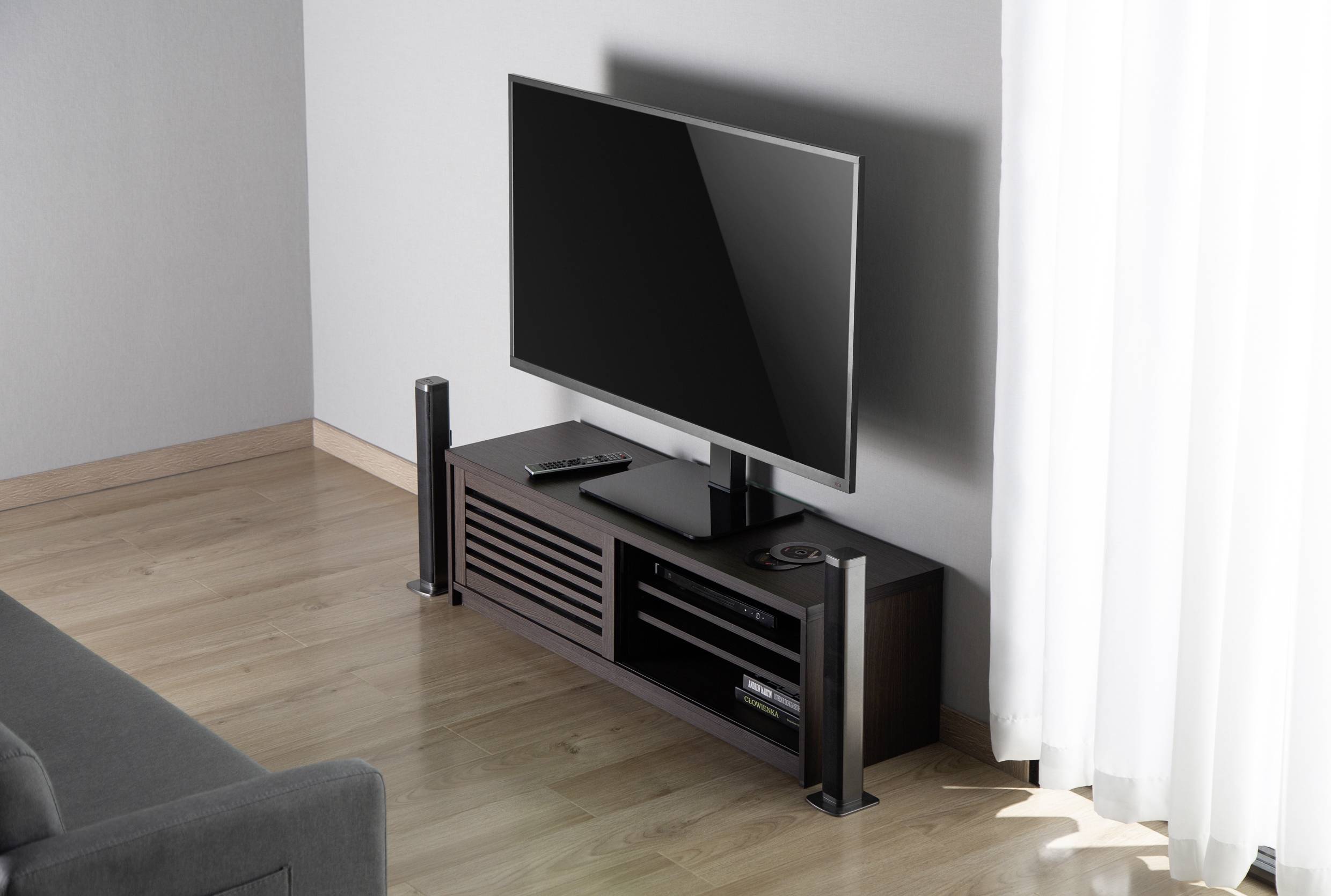 Ein Flachbildfernseher auf einem dunklen, modernen TV-Schrank mit Lautsprechern und Fernbedienung in einem hellen, minimalistischen Wohnzimmer.