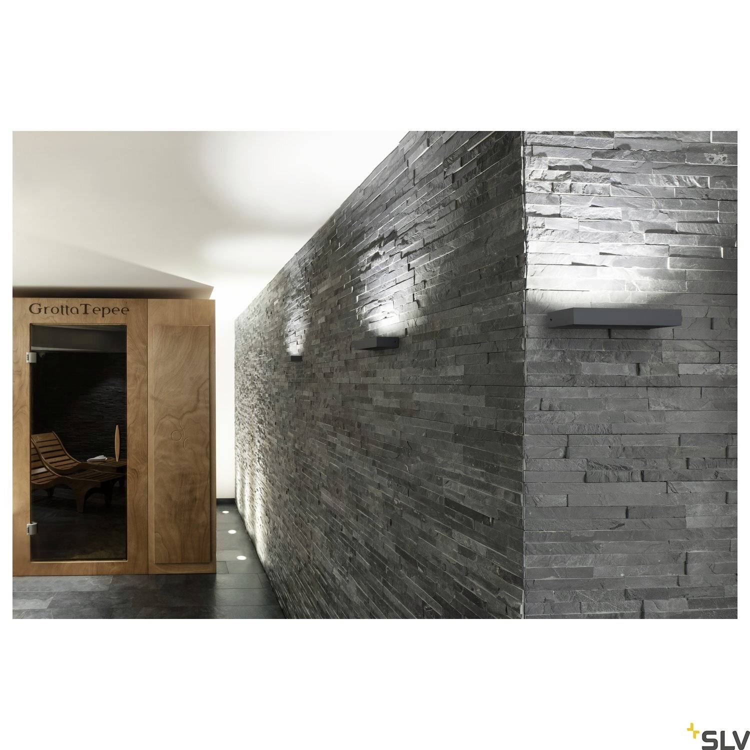 Ein moderner Wellnessbereich mit einer Sauna aus Holz auf der linken Seite und einer grauen Steinwand mit sanfter Beleuchtung rechts.