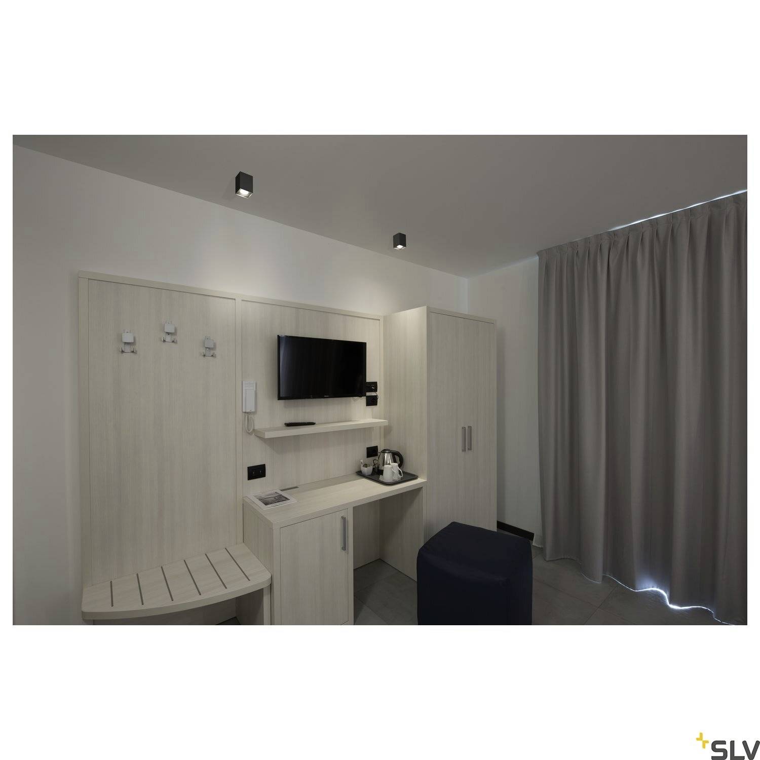 Ein Hotelzimmer mit modernem Design. Es gibt einen Kleiderschrank, eine Sitzecke, einen Fernseher an der Wand, einen Safe und einen Wasserkocher.
