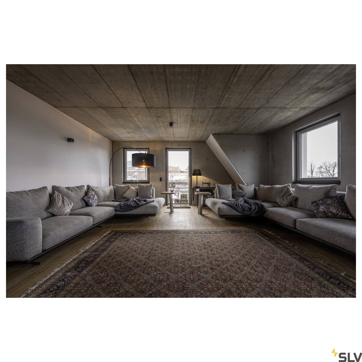 Großes, modernes Wohnzimmer mit grauen Sofas, Teppich und Fenstern. Minimalistisches Design mit einem Couchtisch und Lampe in der Mitte.