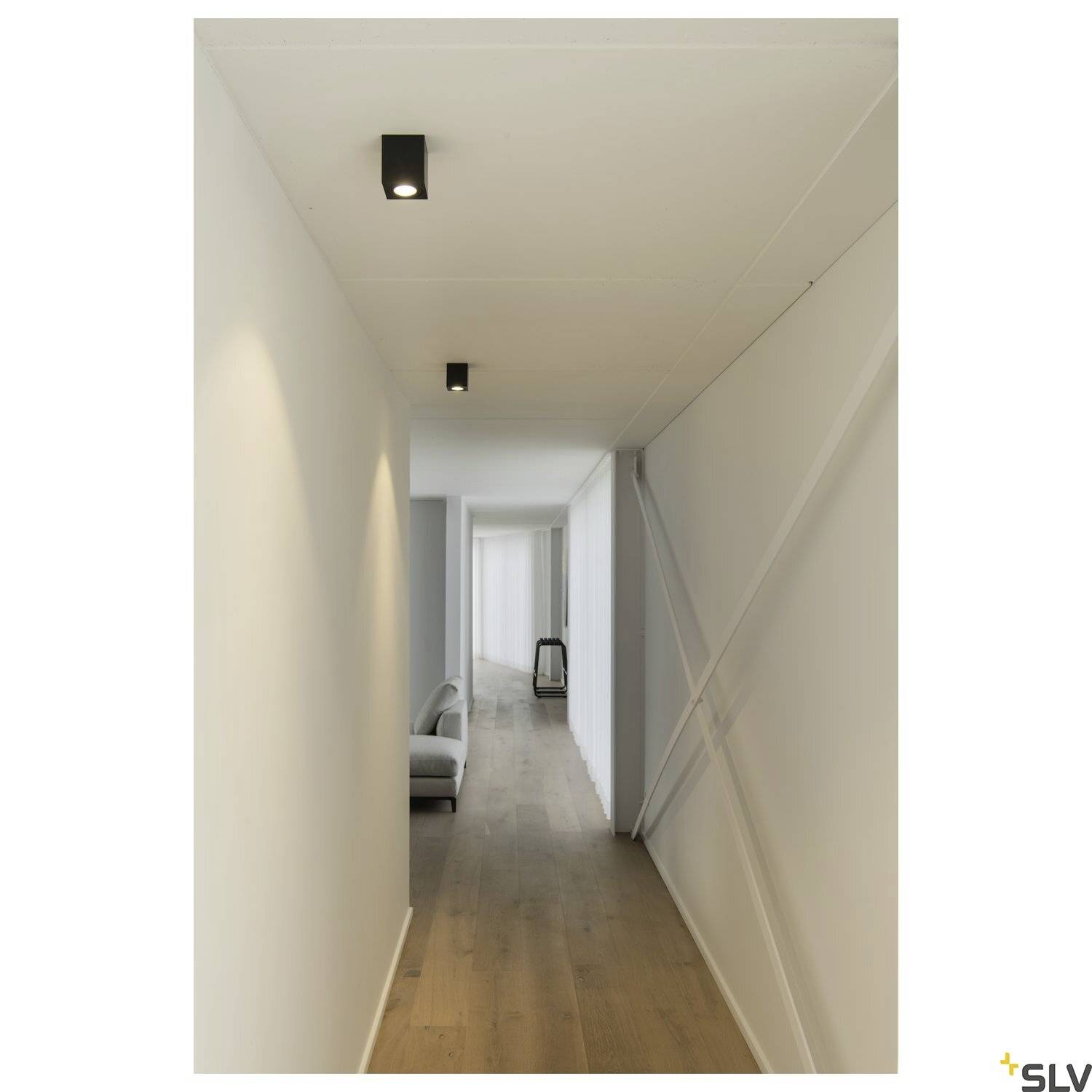 Langer, schmaler Flur mit Holzboden und Deckenleuchten. Wände sind weiß gestrichen, modernes minimalistisches Design.