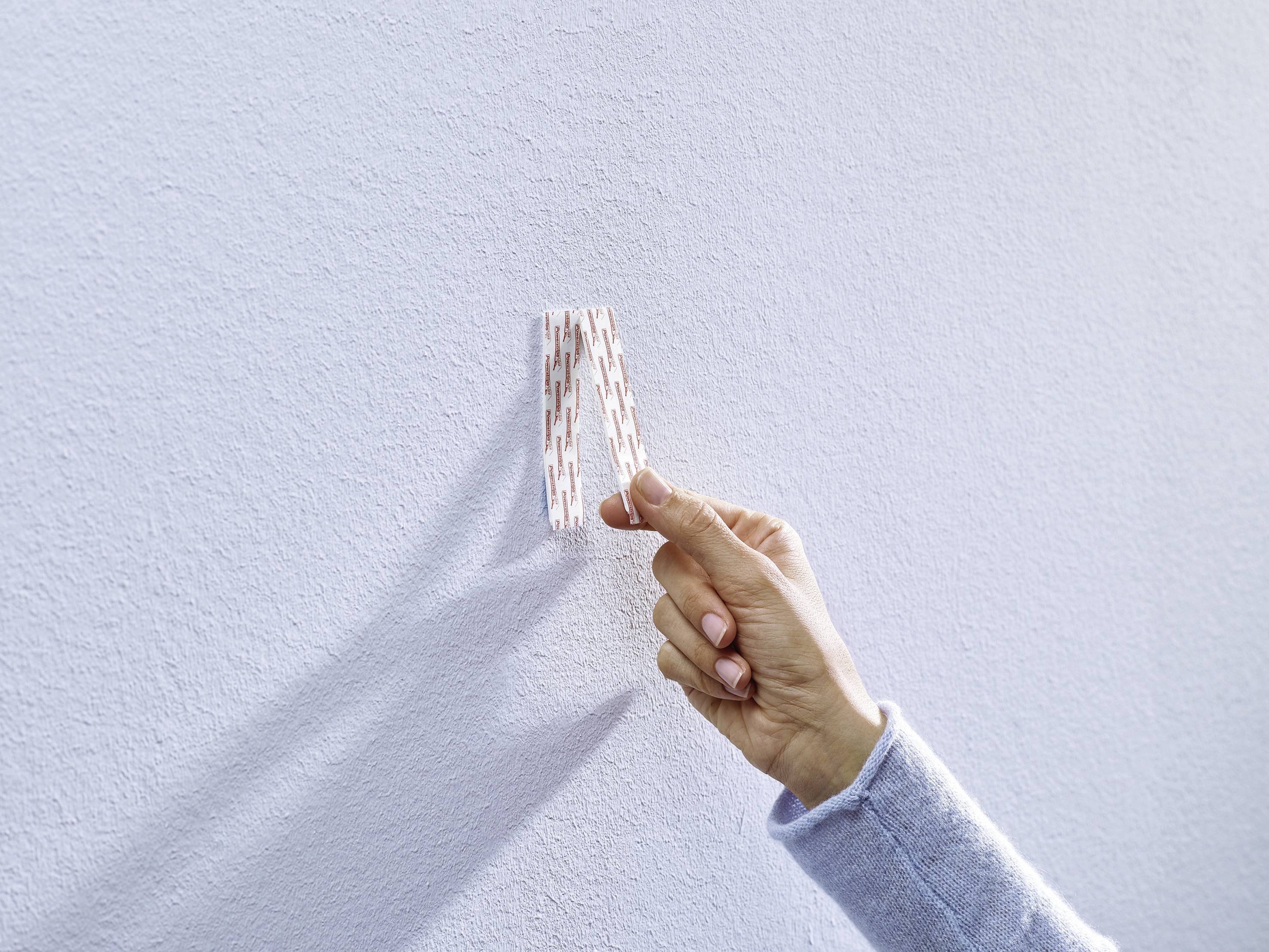 Hand platziert selbstklebenden Streifen an einer weißen Wand.