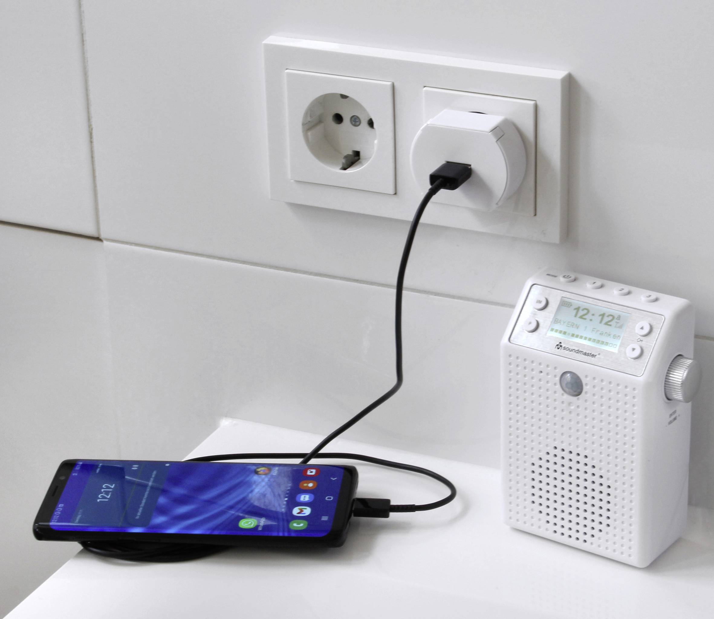 Ein Smartphone wird über ein USB-Kabel an ein Steckdosenradio angeschlossen, das selbst an eine Steckdose angeschlossen ist.