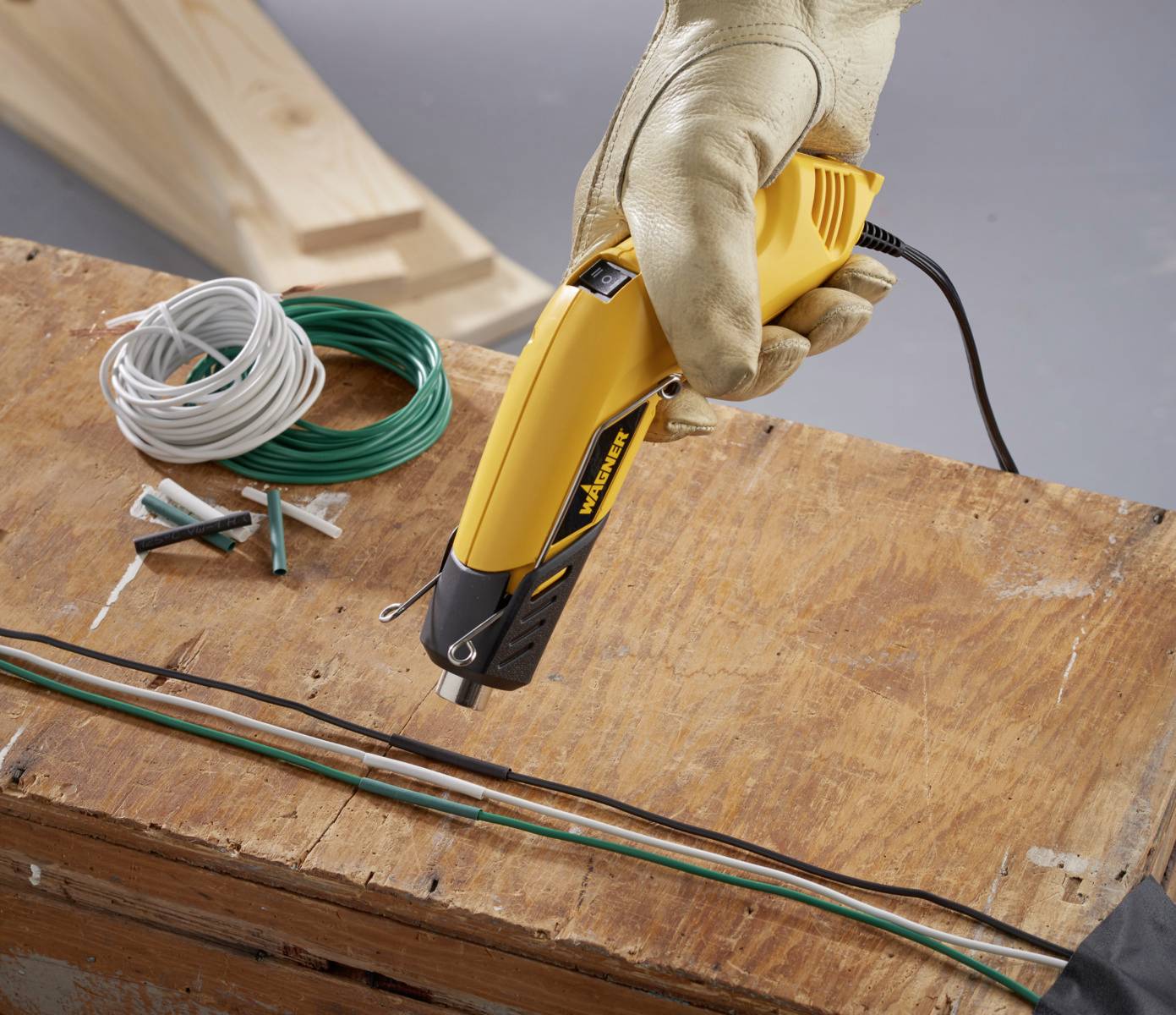 Ein gelber Elektroschneider, gehalten von einer behandschuhten Hand, schneidet Kabel auf einem Holztisch. Daneben liegen zusätzliche Kabel.