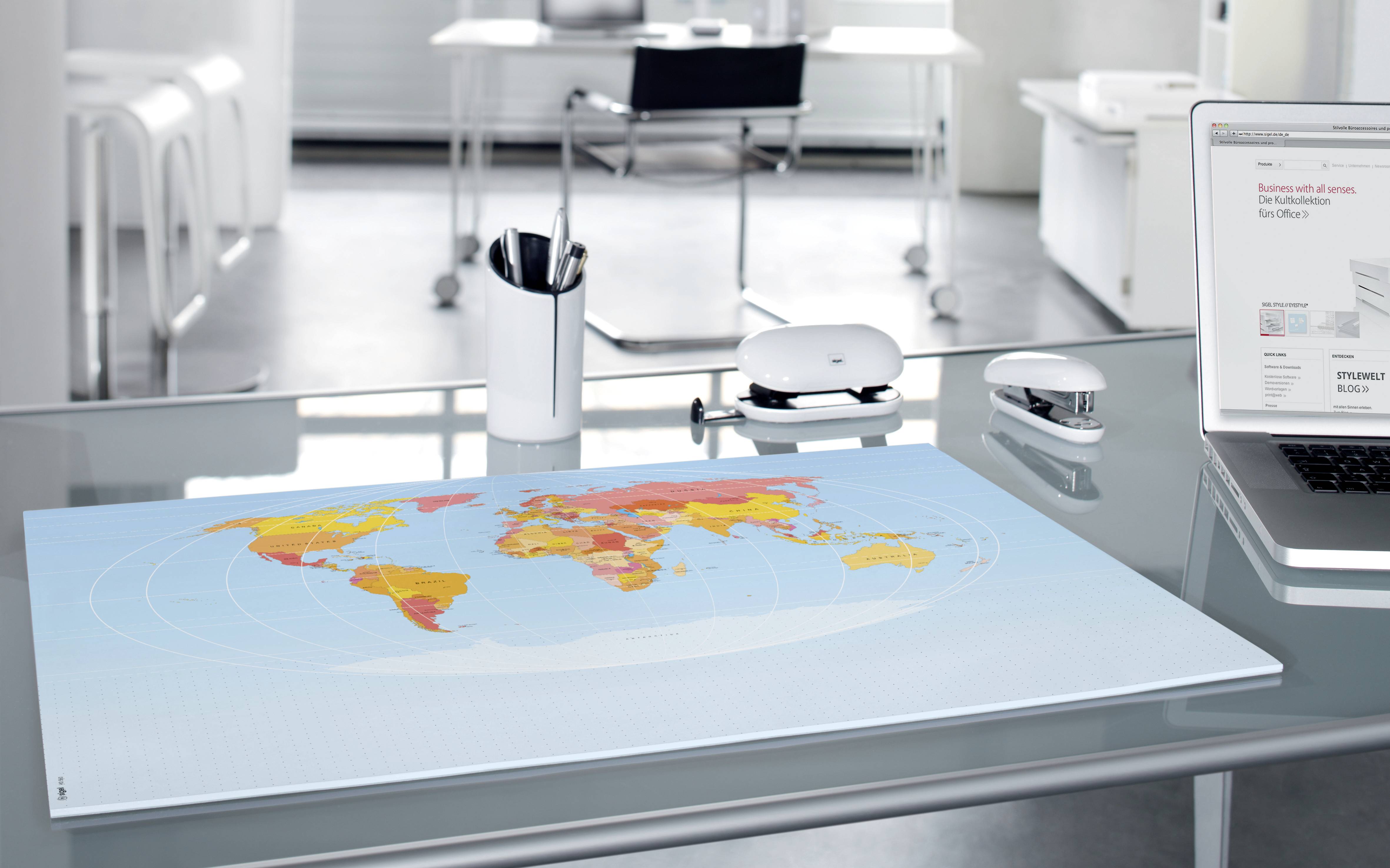 Büro mit modernem Schreibtisch, auf dem eine Weltkarte liegt. Laptop geöffnet mit einer Webseite sichtbar; Hintergrund mit Büromöbeln.