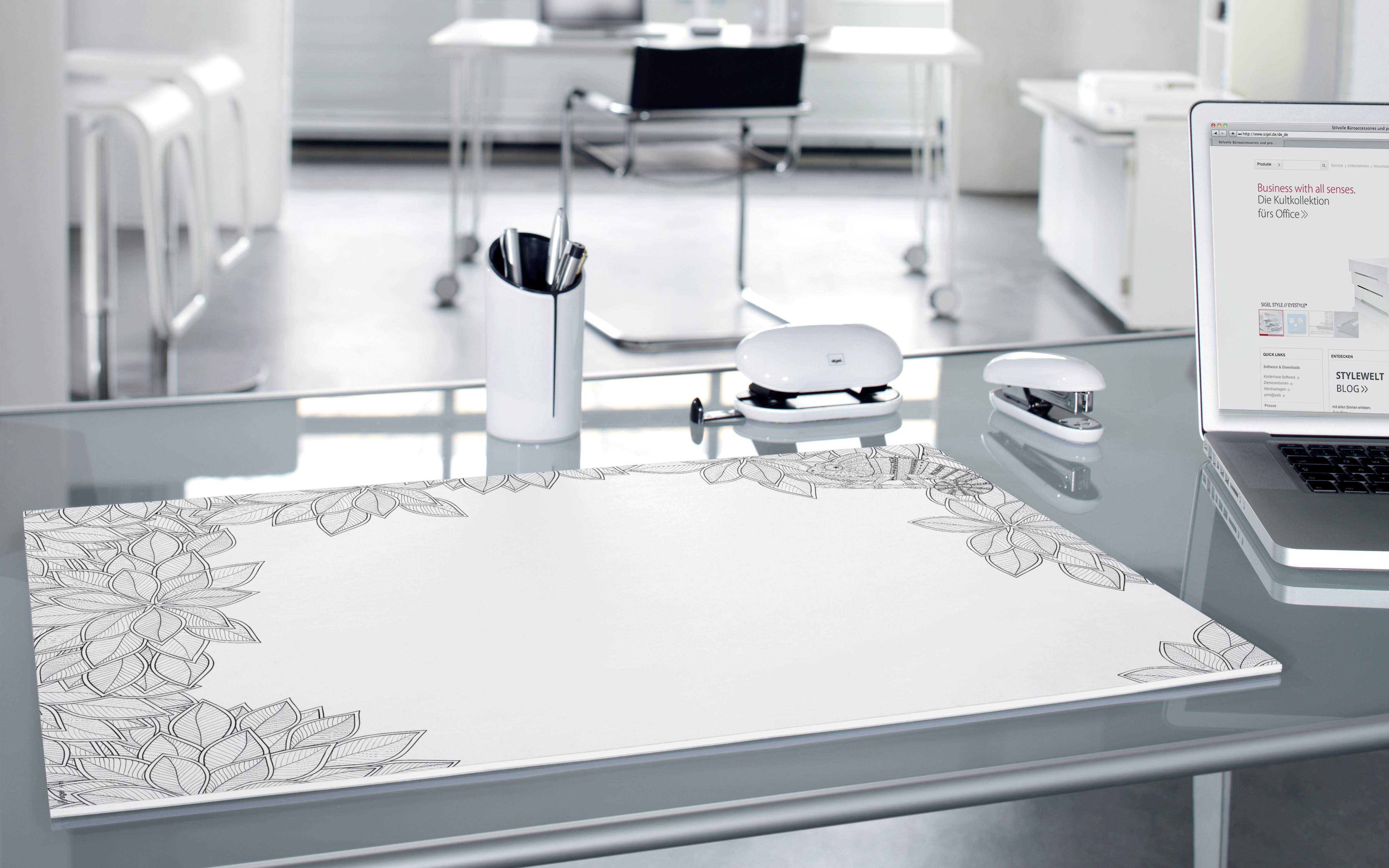 Ein moderner, leerer Schreibtisch mit einem Laptop, einem Tischkalender und Stiften in einem Becher in einem hellen Büro.