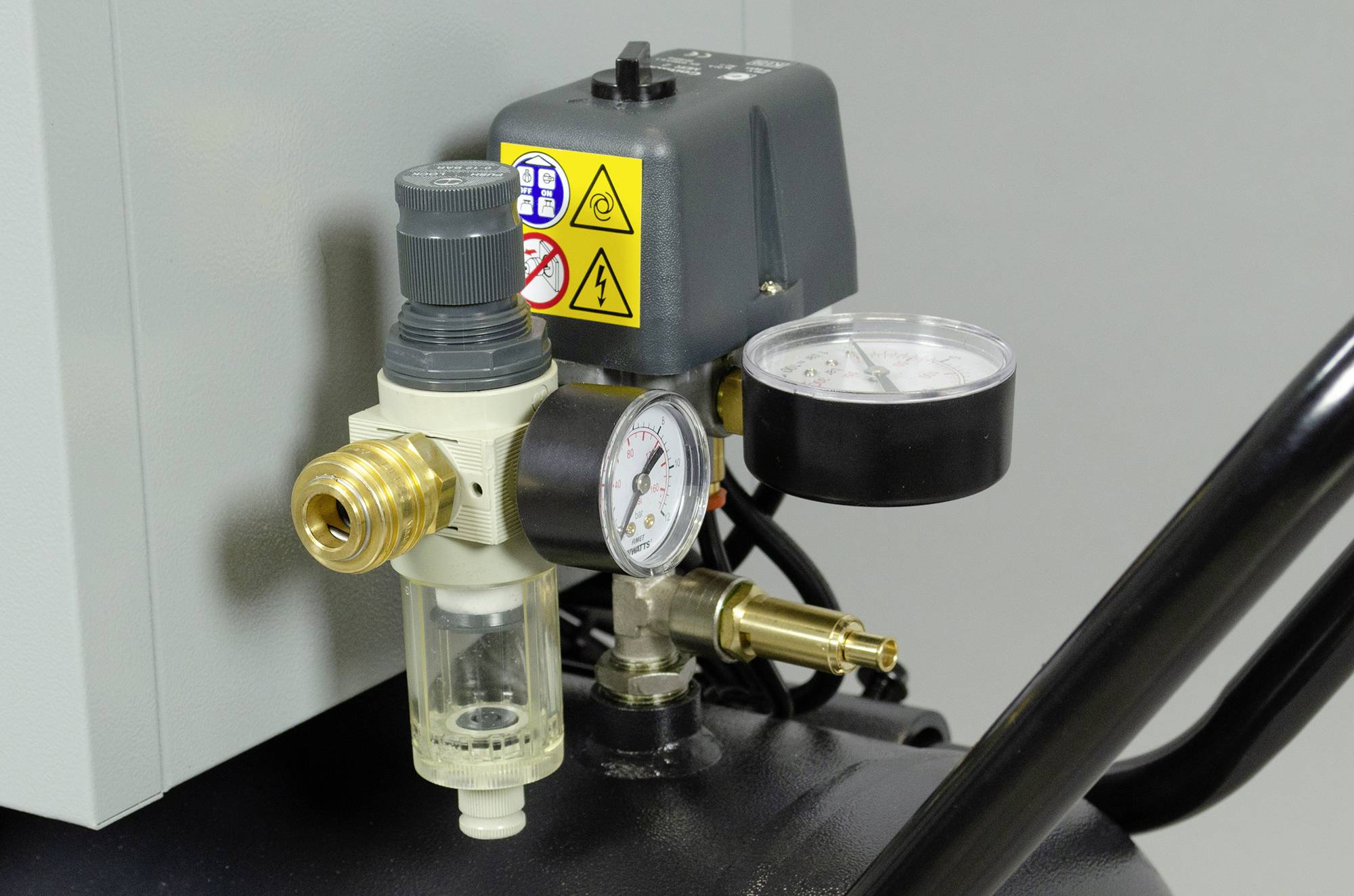 Manometer und Druckregler an einem Druckluftkompressor, Anzeige zeigt aktuellen Druck an. Wichtige Warnhinweise auf dem Gerät.