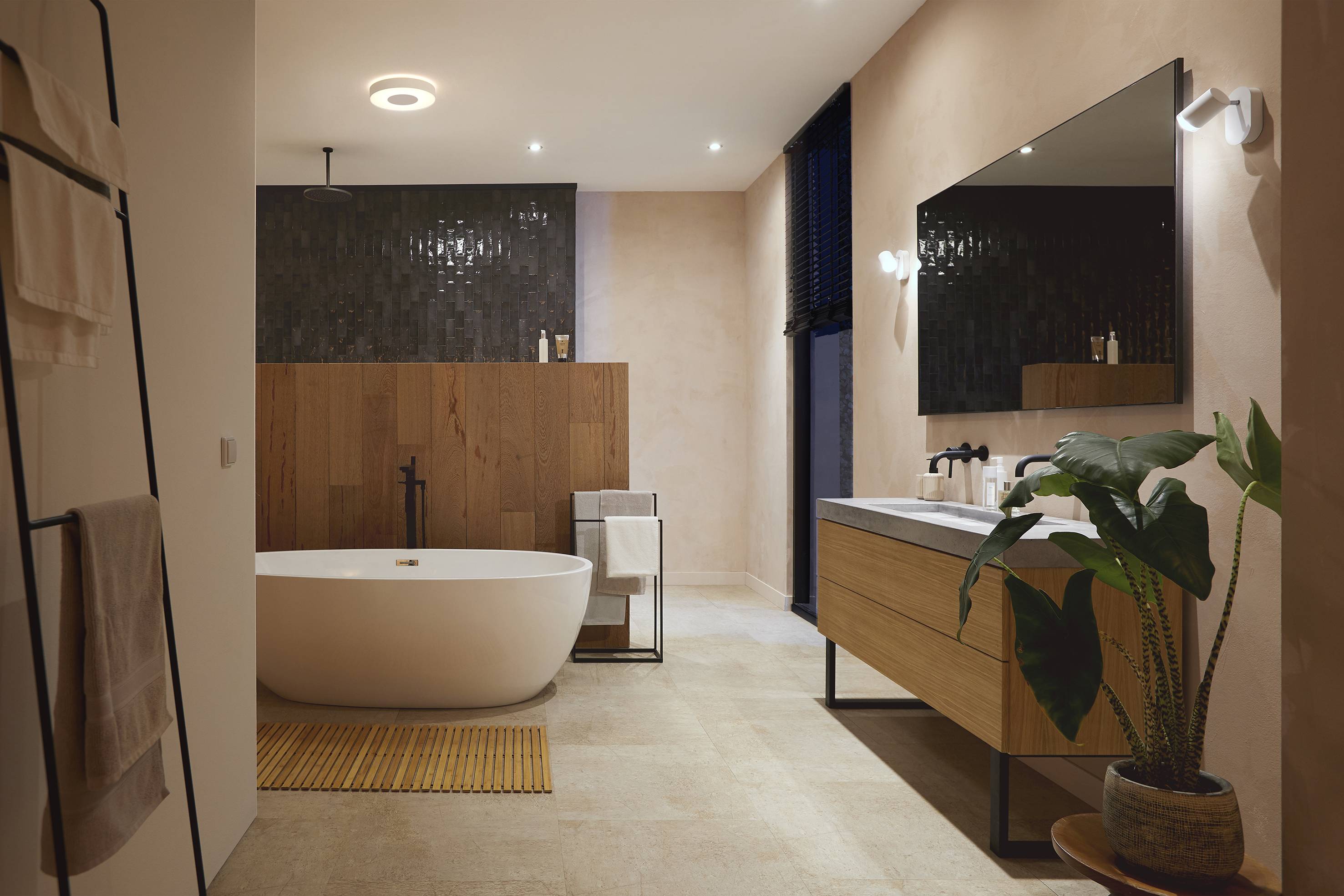 Modernes Badezimmer mit freistehender Badewanne, Holzverkleidung, großem Spiegel und Waschbecken; Pflanzen- und Dekorelemente ergänzen das Design.