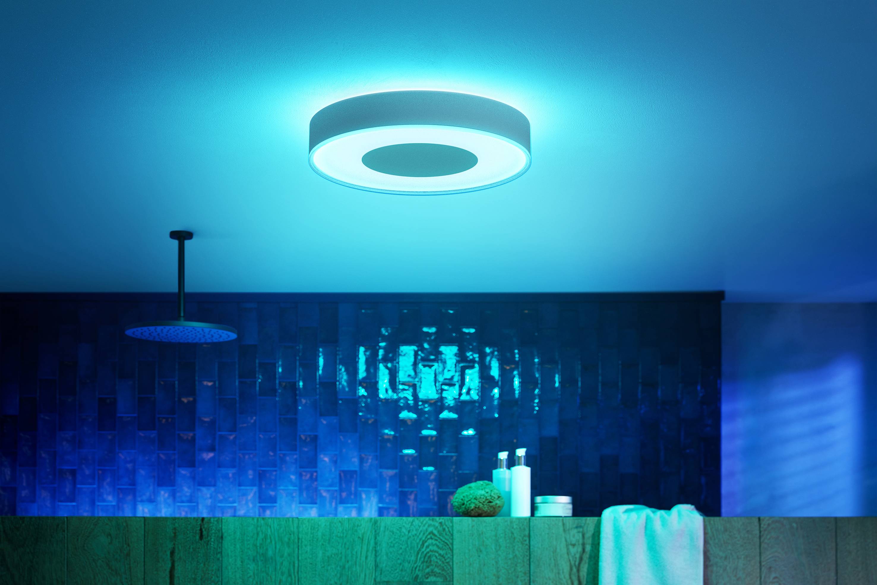 Ein Badezimmer mit blauen Fliesen und gedimmter Beleuchtung von einer runden Deckenlampe, die ein beruhigendes Ambiente schafft.