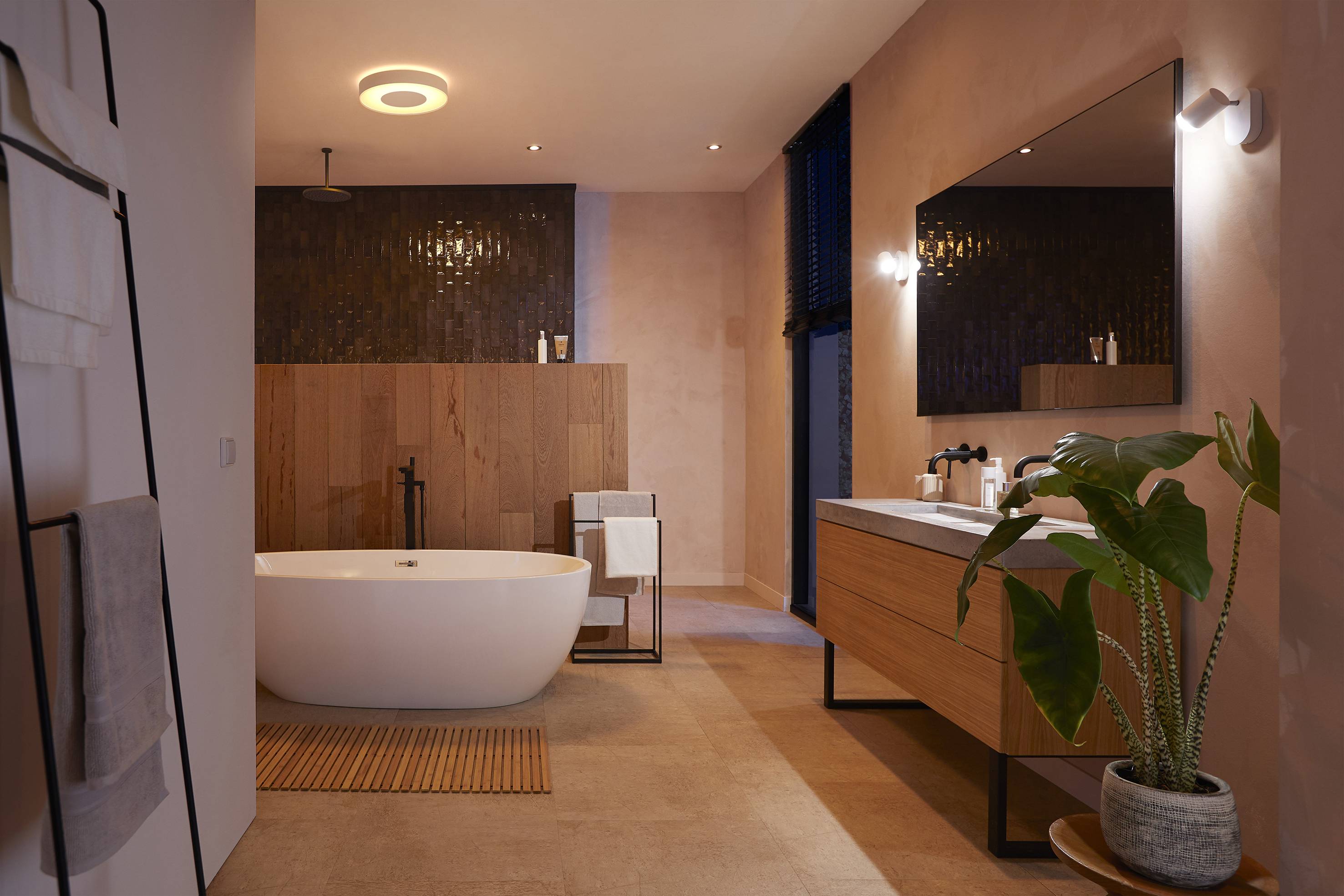 Modernes Badezimmer mit freistehender Badewanne, Holzverkleidung an der Wand, großem Spiegel, Waschtisch aus Holz und Zimmerpflanze.