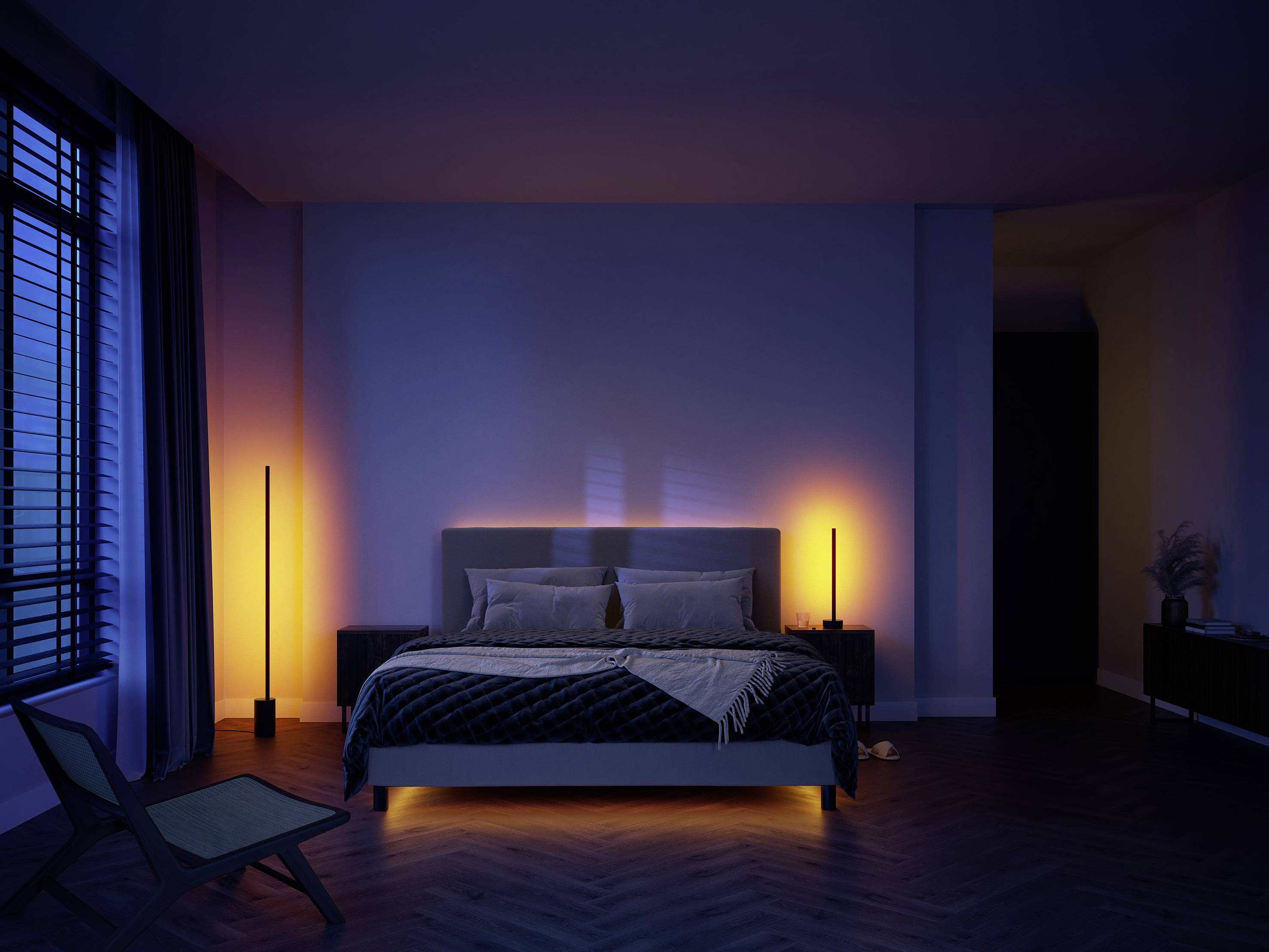Ein Schlafzimmer mit einem großen Bett, von warmem Licht beleuchtet. Links stehen zwei hohe Lampen. Rechts ein Stuhl vor einem Fenster.