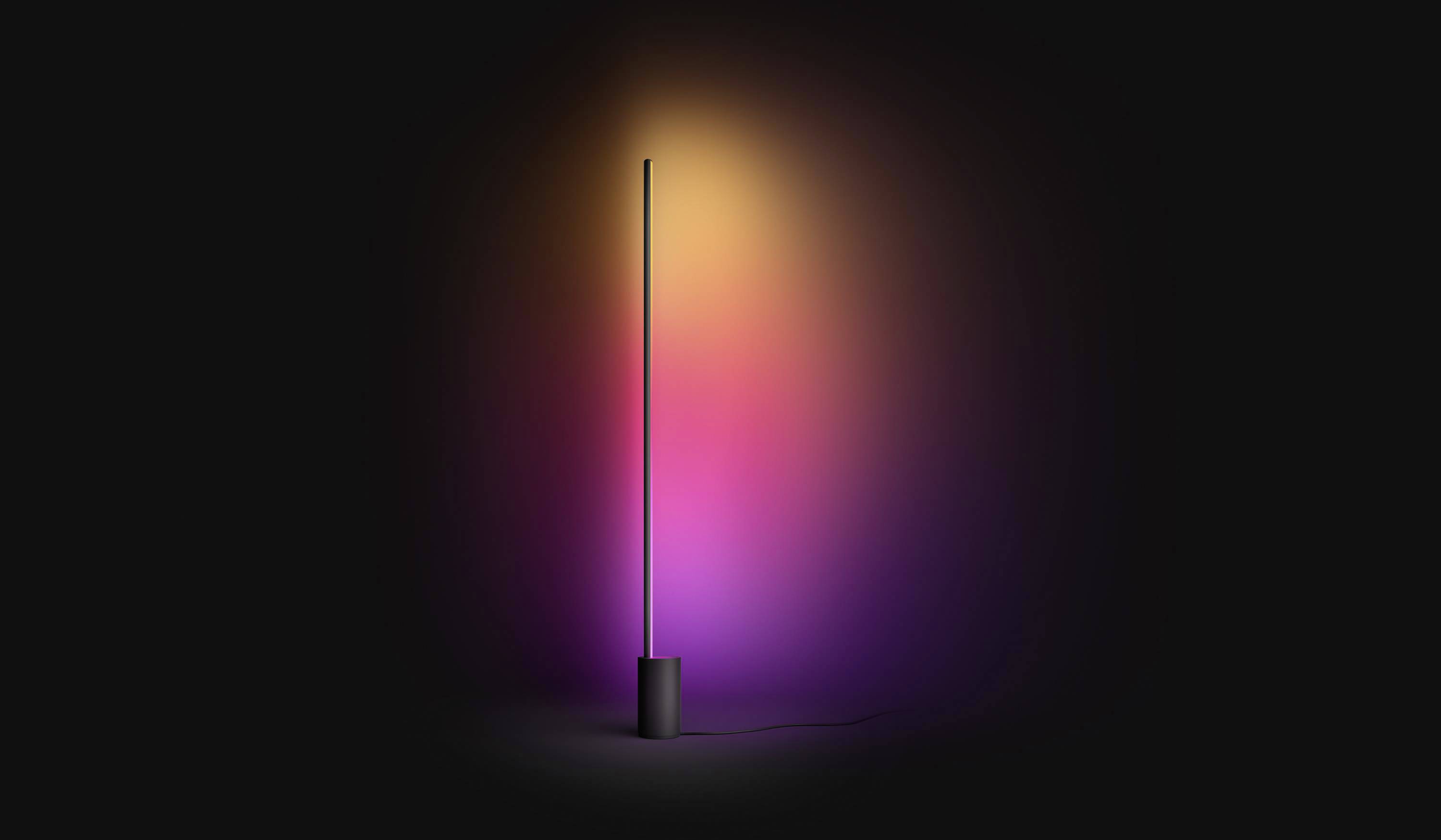 Stehlampe mit langem, schlankem Stab strahlt mehrfarbiges Licht in Gelb, Orange und Violett in dunklem Raum aus. Modernes, minimalistisches Design.