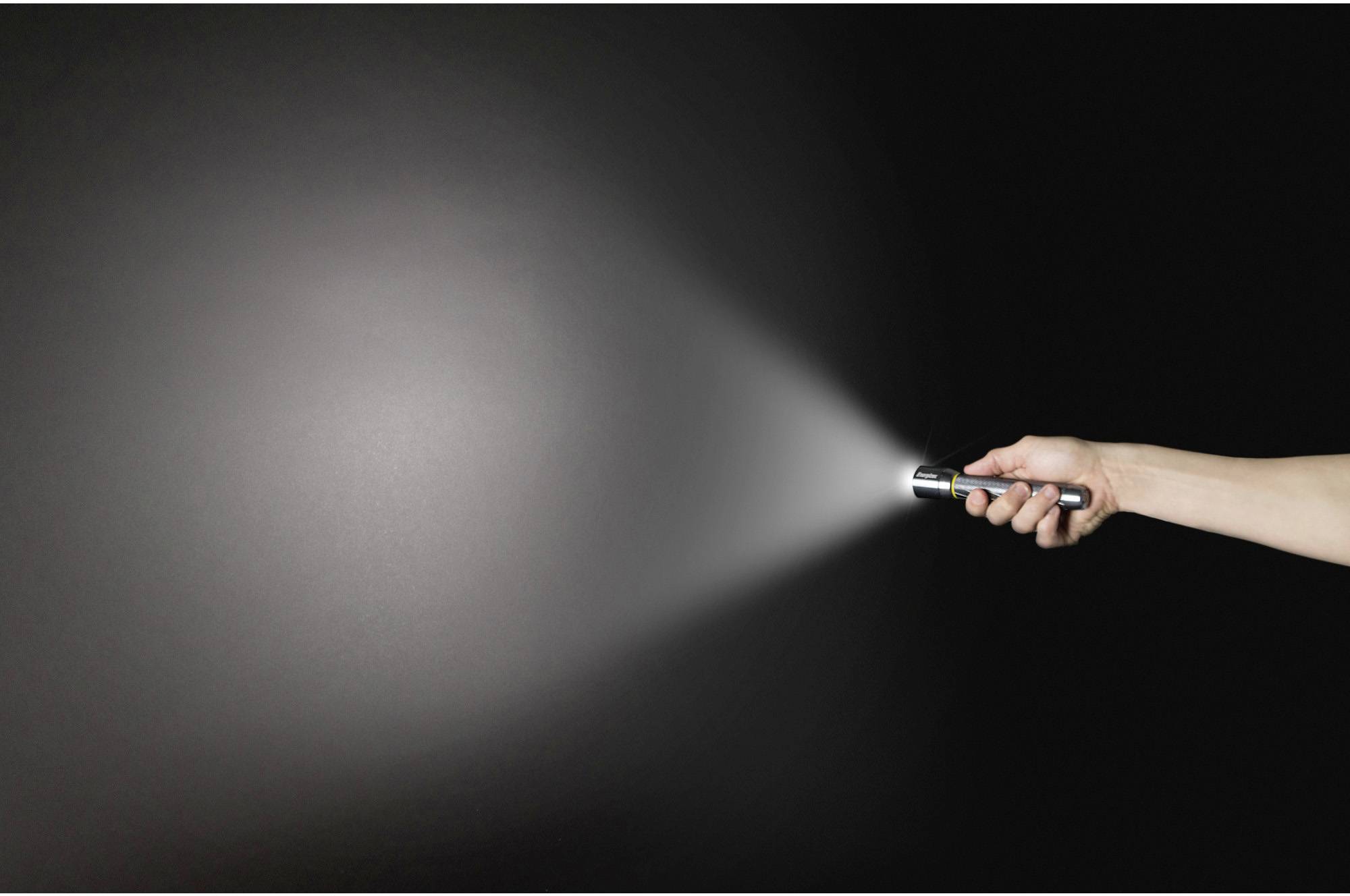 Eine Hand hält eine Taschenlampe und strahlt Licht auf eine dunkle Fläche.