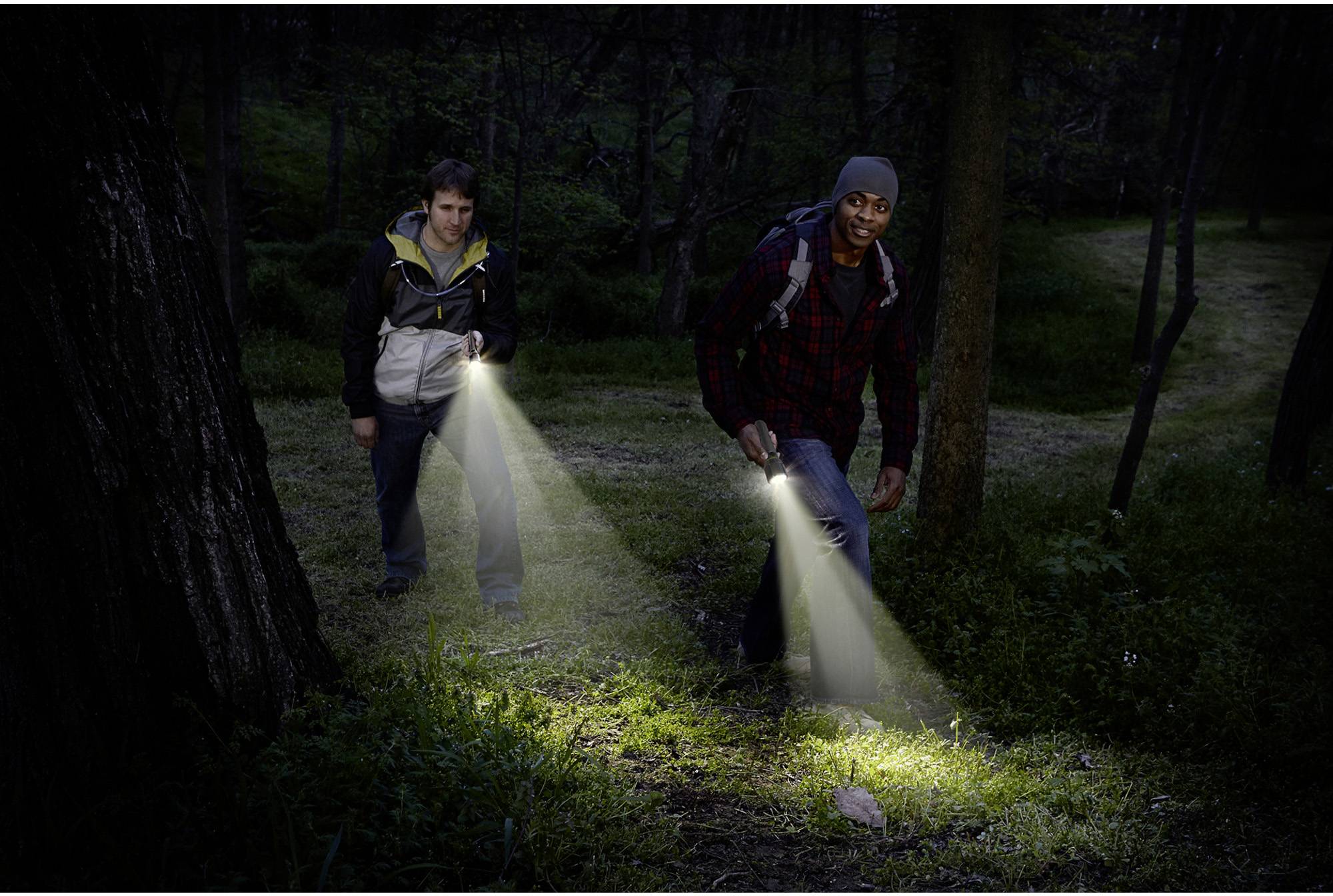 Zwei Personen gehen nachts durch einen Wald und leuchten mit Taschenlampen auf den Boden.