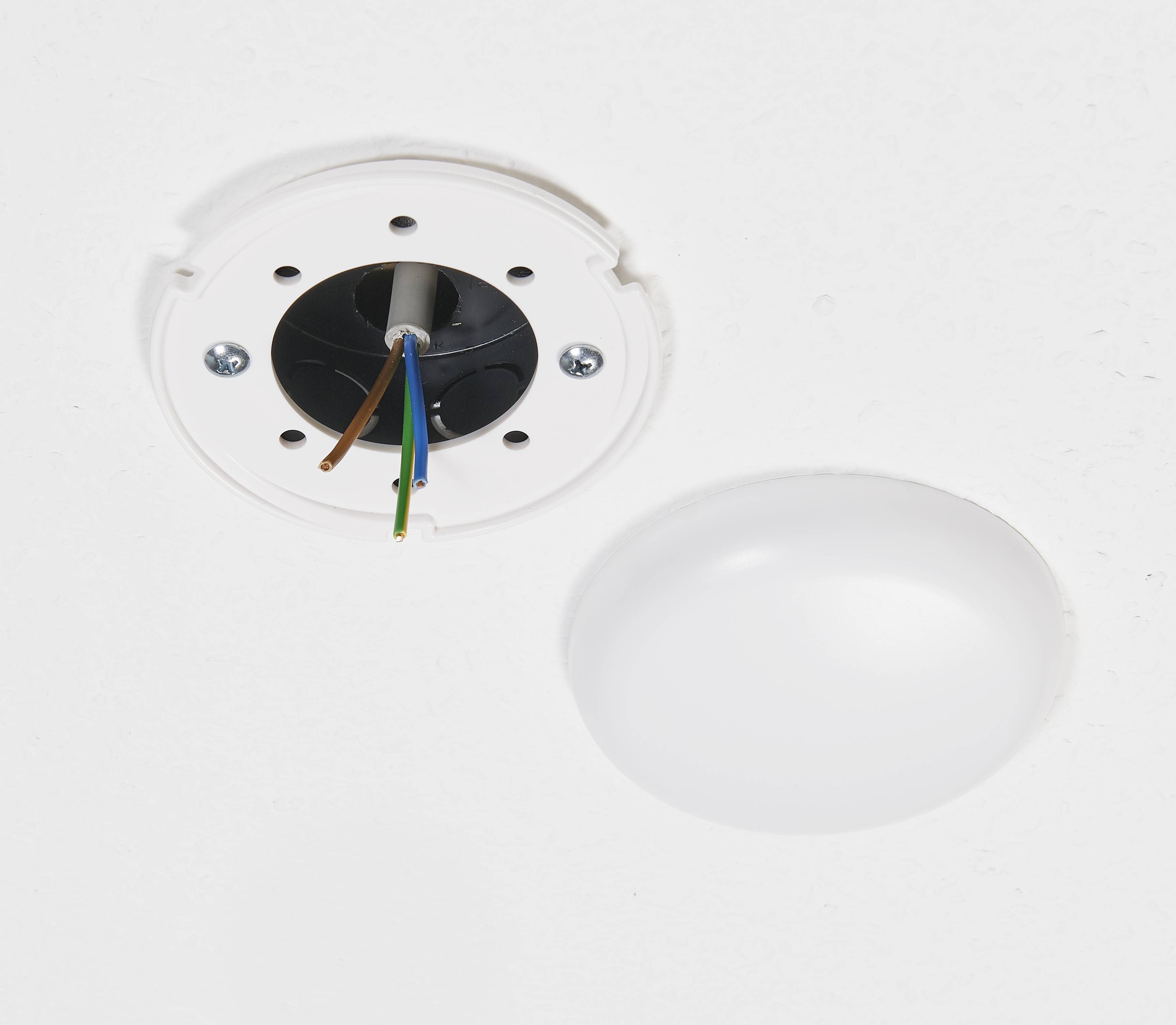 Eine abgenommene Deckenlampe zeigt freiliegende Drähte an der Decke, daneben die abgenommene Lampenabdeckung.