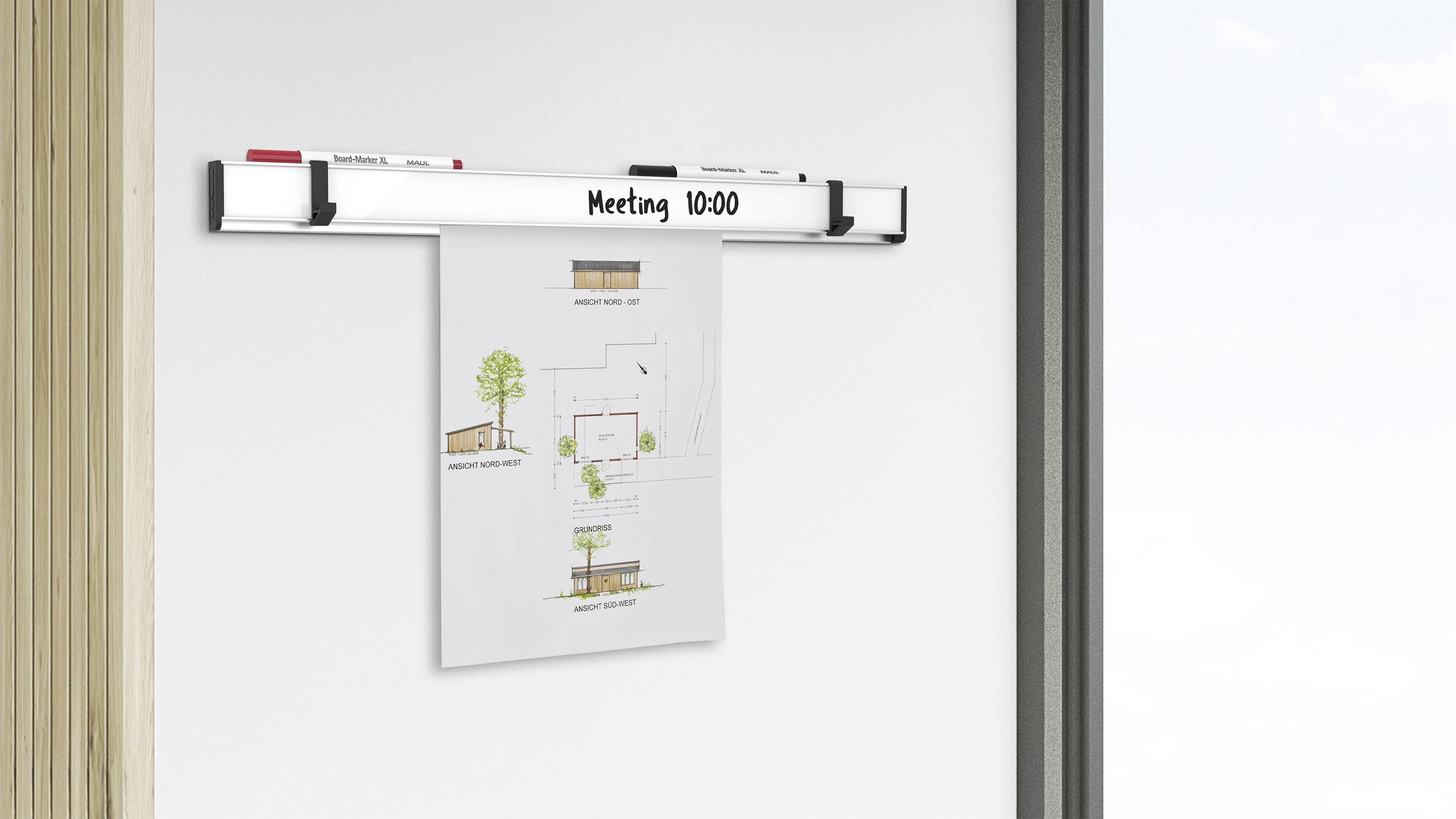 Magnetische Halterung mit Papierhalterung an der Wand zeigt einen Architekturplan, Aufschrift 'Meeting 10:00', daneben ein Whiteboard-Marker.