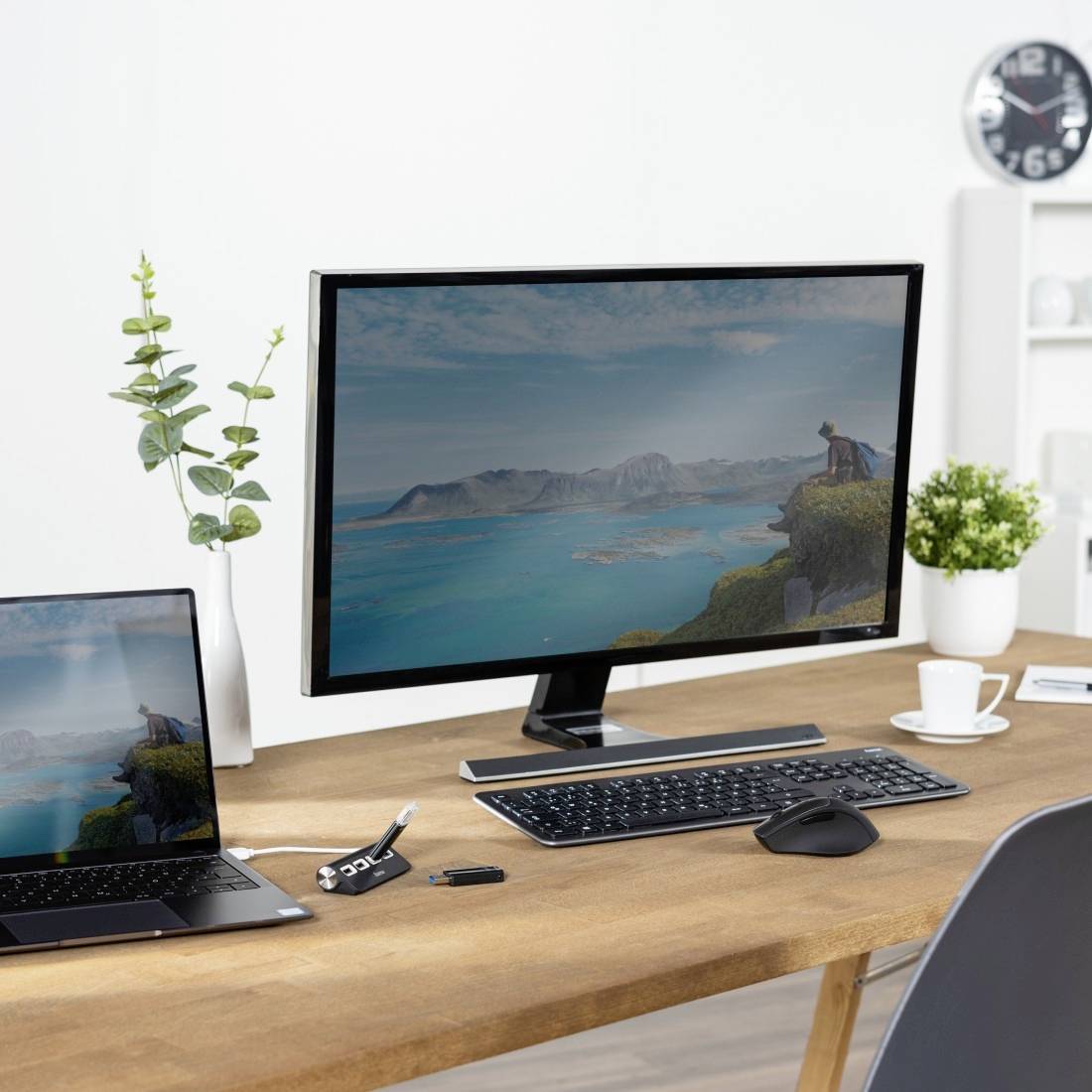 Zwei Monitore auf einem Schreibtisch zeigen eine Landschaft mit Meer und Bergen. Daneben stehen eine Tastatur, Maus und ein Laptop.