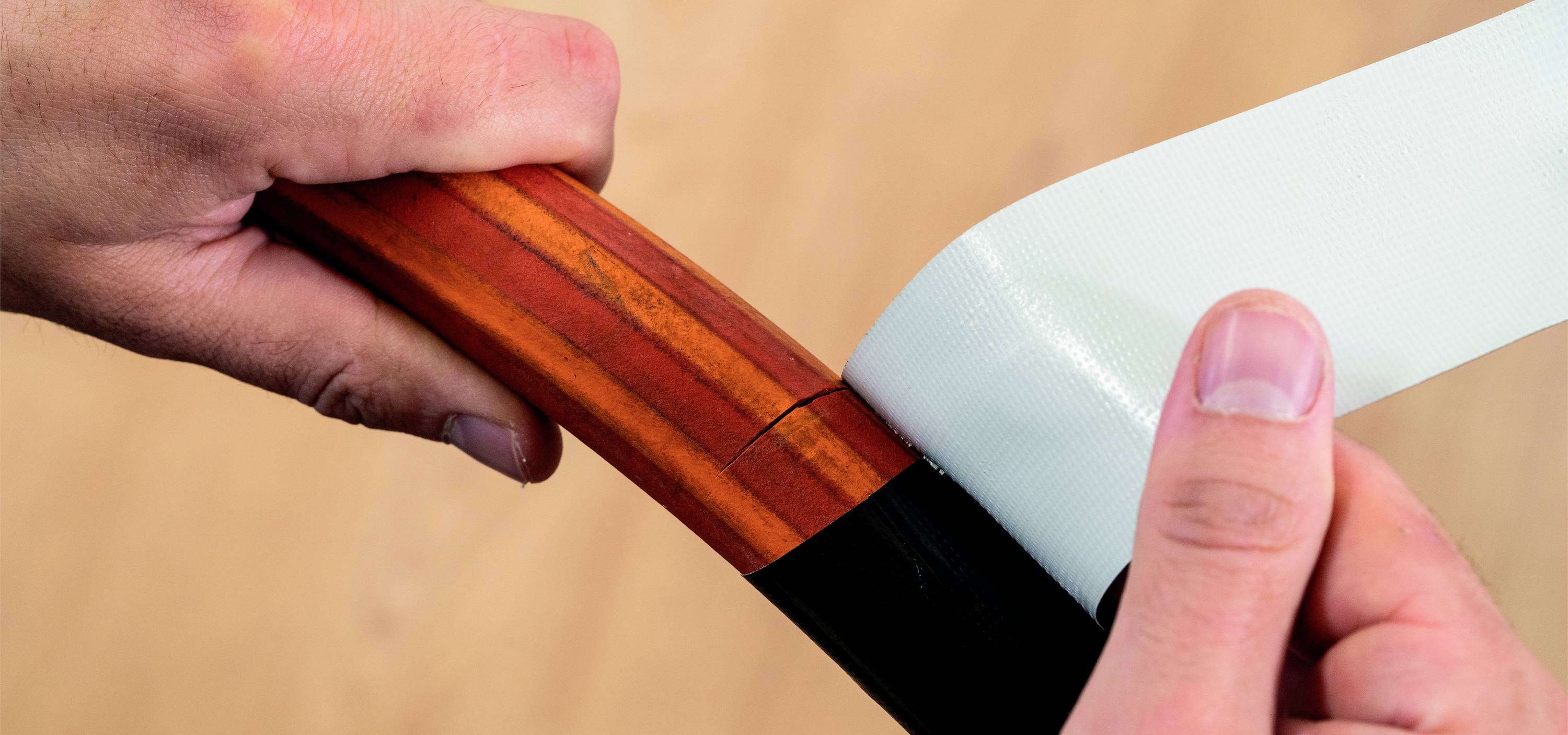 Eine Person umwickelt einen Bogen mit weißem Tape zur Verstärkung oder Reparatur. Der Bogen hat eine dunkelbraune Farbe.
