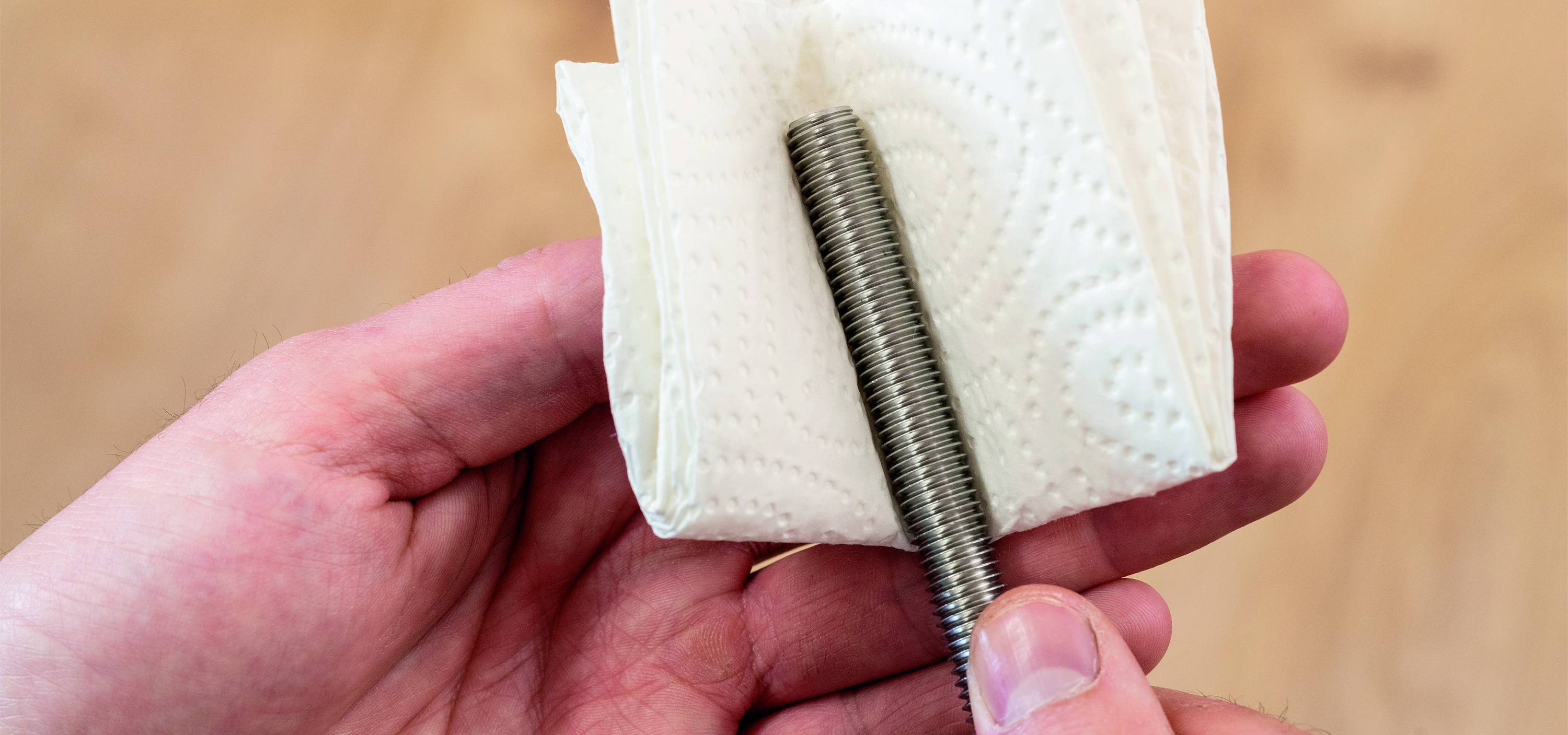 Hand hält eine Schraube in ein gefaltetes Papiertuch gewickelt.