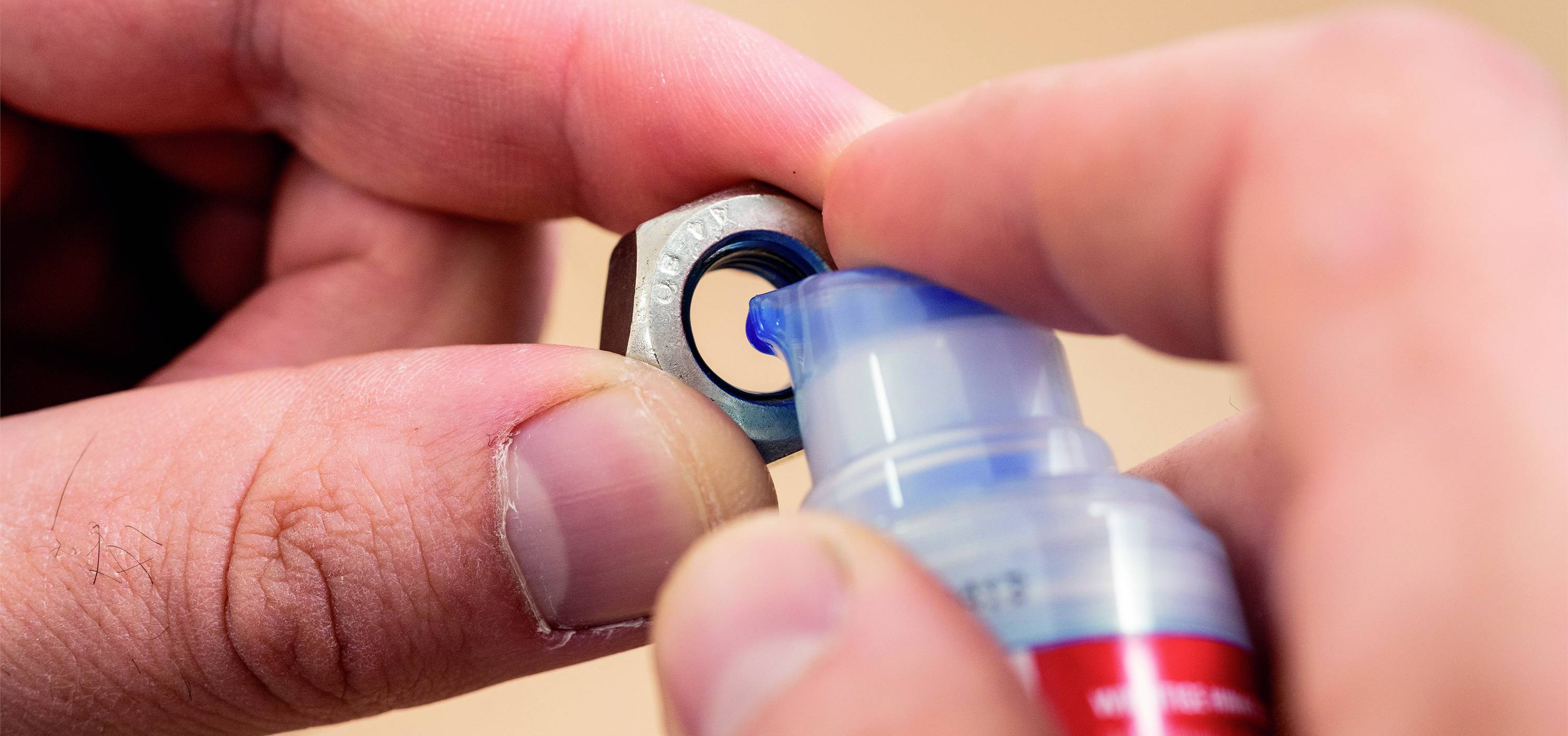 Eine Person trägt mit einer Flasche blaue Schraubensicherungslösung auf eine Metallmutter auf.