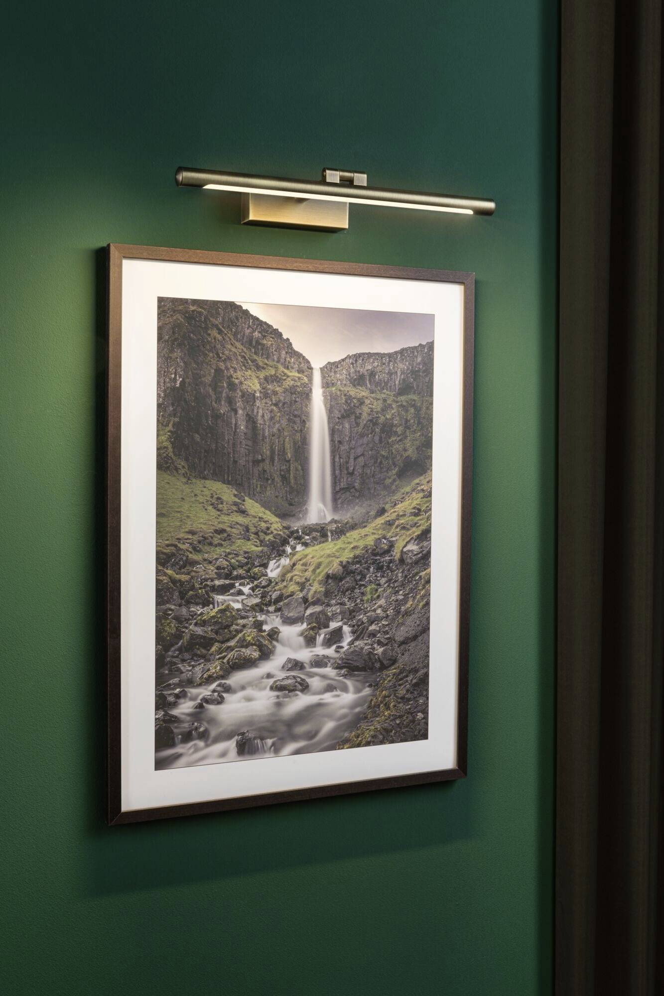 Ein gerahmtes Foto eines Wasserfalls hängt an einer grünen Wand. Das Bild zeigt einen hohen Wasserfall, der über Felsen hinabstürzt.
