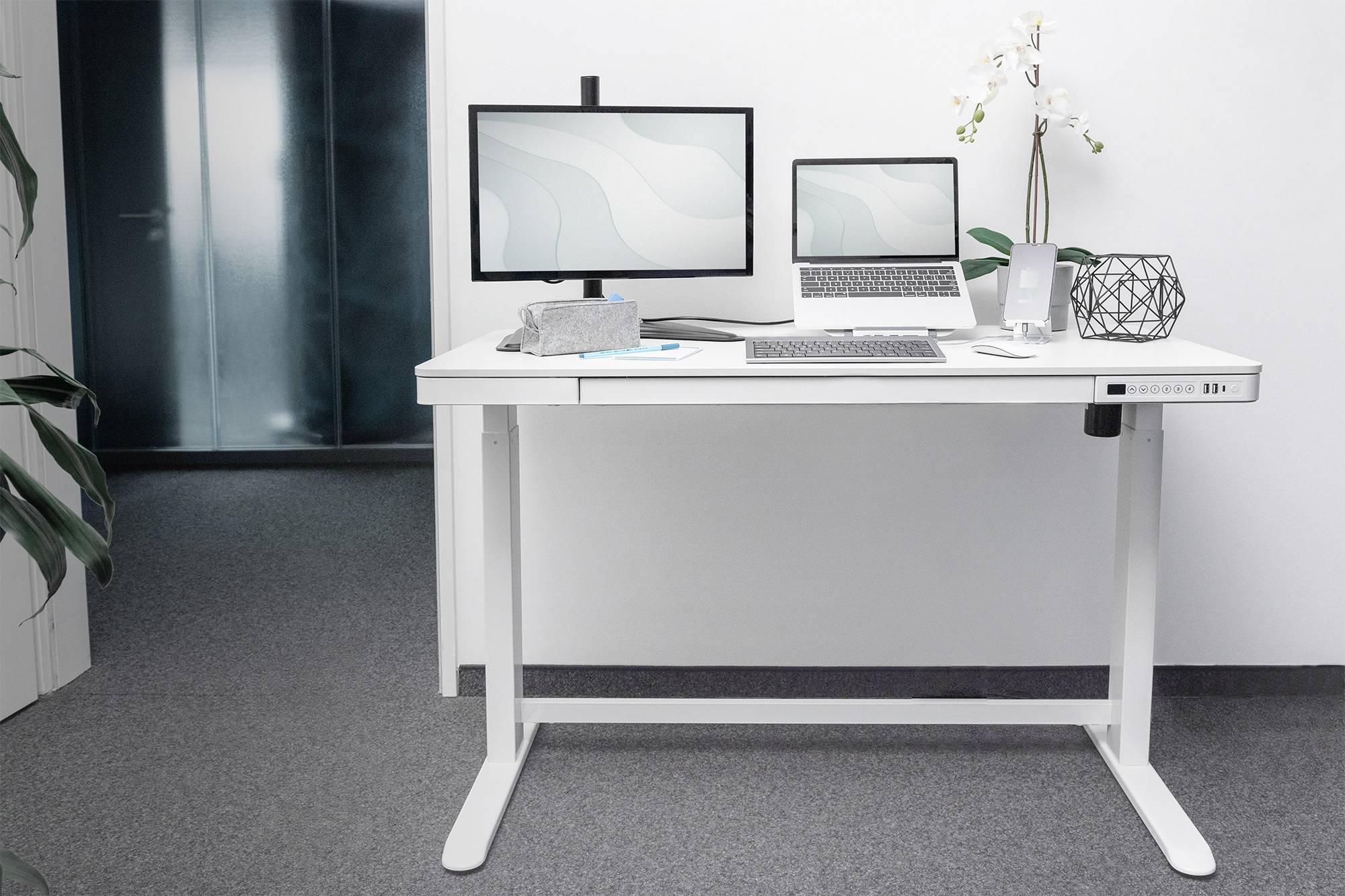 Ein moderner Stehschreibtisch mit Laptop, zwei Monitoren, Tastatur und Dekorationen wie eine Pflanze in einem Büro.