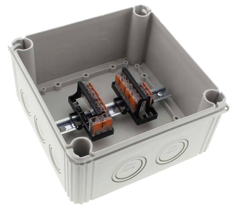 Graues, leeres elektrisches Anschlussgehäuse mit zwei orange-schwarzen Klemmen auf einer Metallschiene montiert.