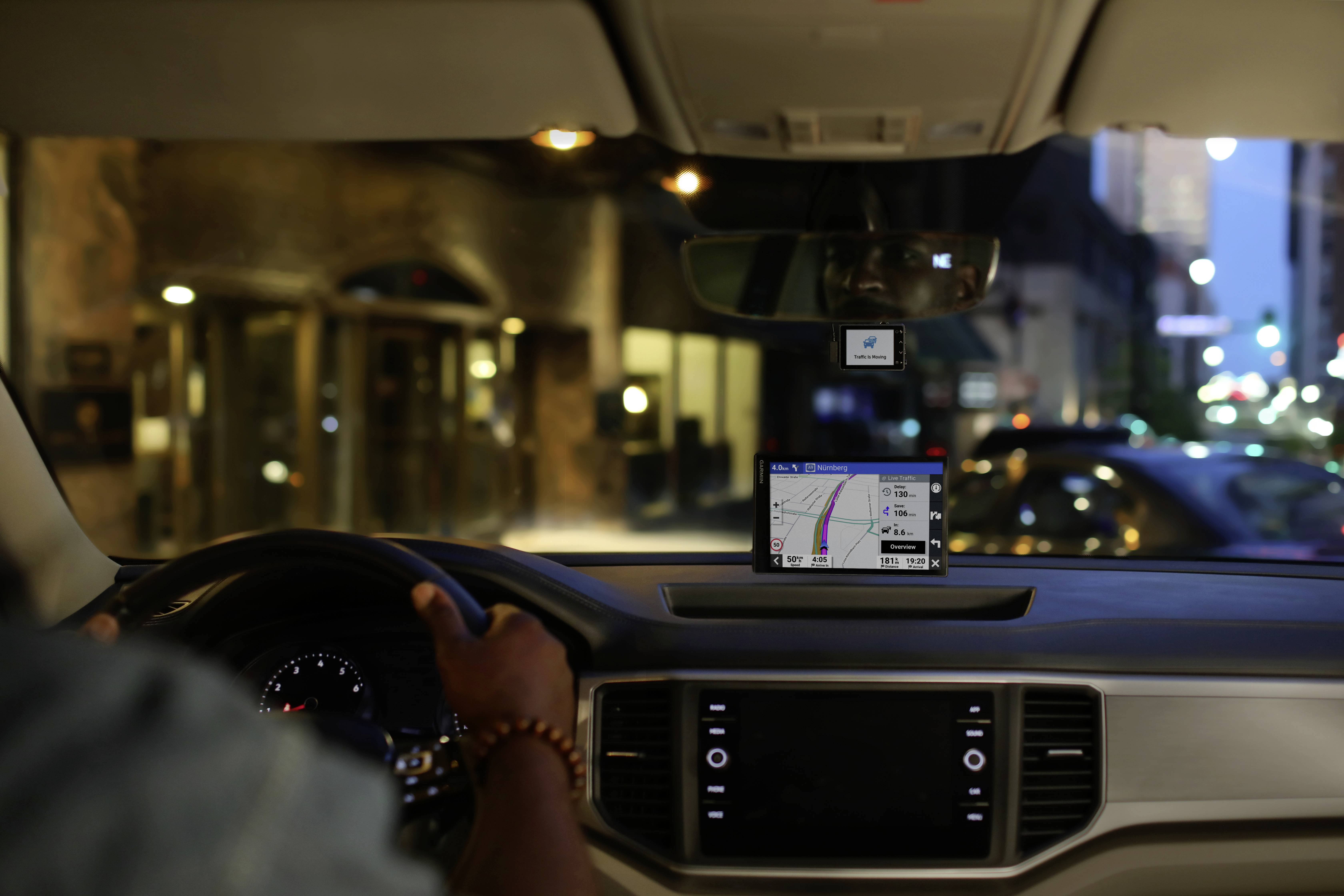 Ein Autofahrer navigiert nachts eine Stadtstraße mit einem GPS-System auf dem Armaturenbrett. Lichter und Gebäude sind im Hintergrund sichtbar.