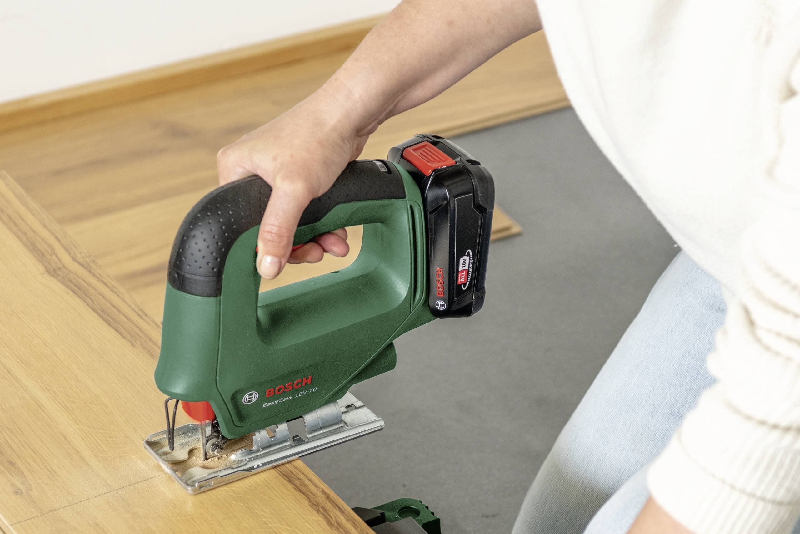 Person schneidet mit einer grünen Bosch-Stichsäge ein Holzbrett. Die Stichsäge ist kabellos und wird über Batterie betrieben.