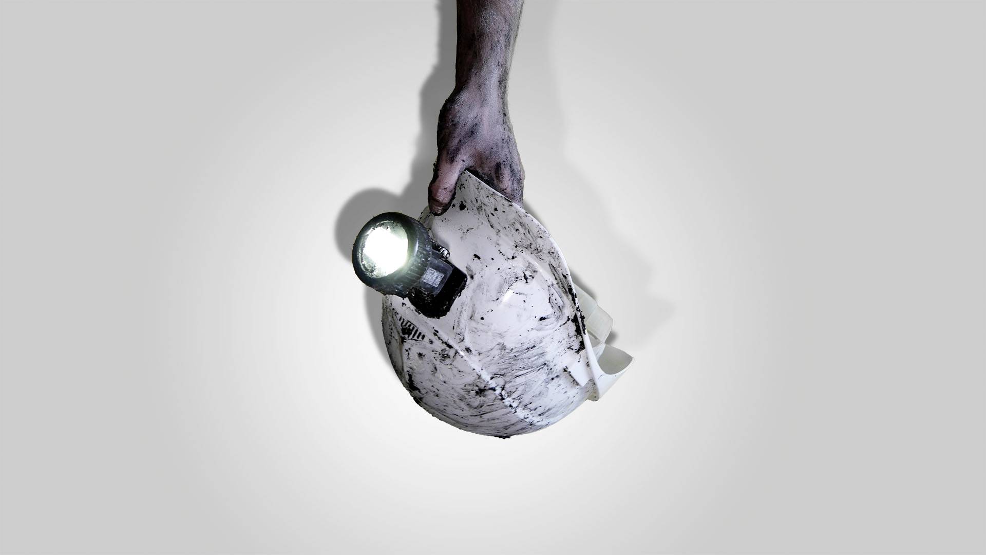 Eine Hand hält einen verschmutzten Bauhelm mit einer leuchtenden Taschenlampe darauf.