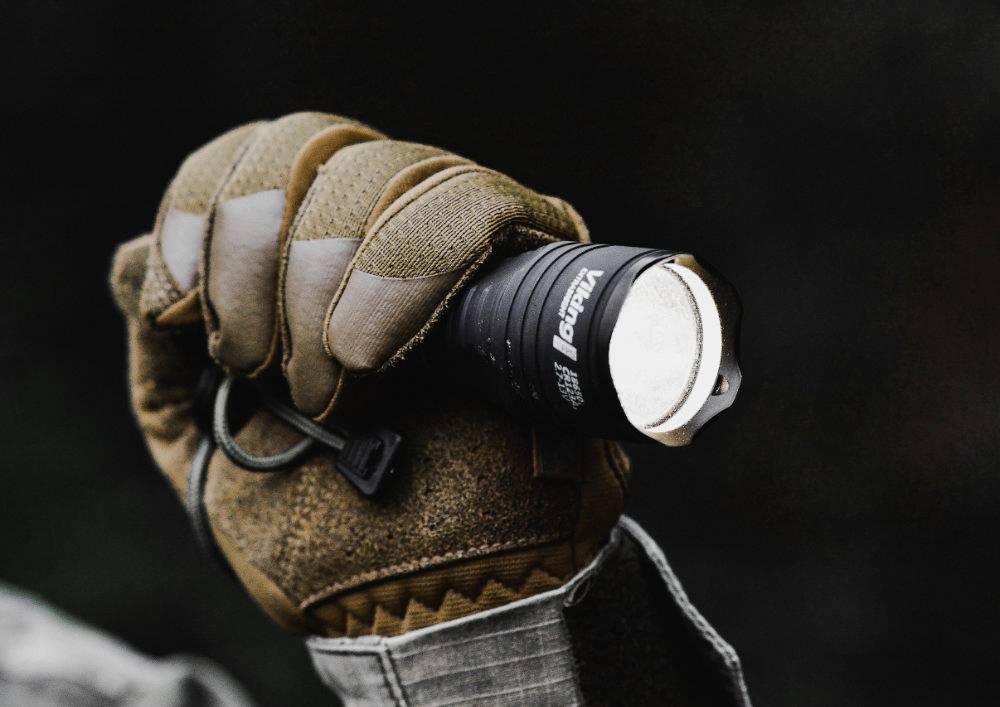 Eine Person hält eine leuchtende Taschenlampe in der Hand, die braun umhüllt ist, mit schwarzem Hintergrund.