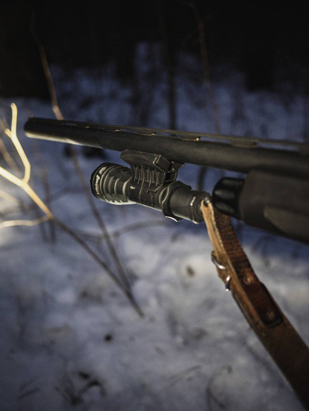 Gewehrlauf im Dunkeln, im verschneiten Wald, mit Taschenlampe montiert, zeigt eine Person auf nächtlicher Jagd oder Patrouille.