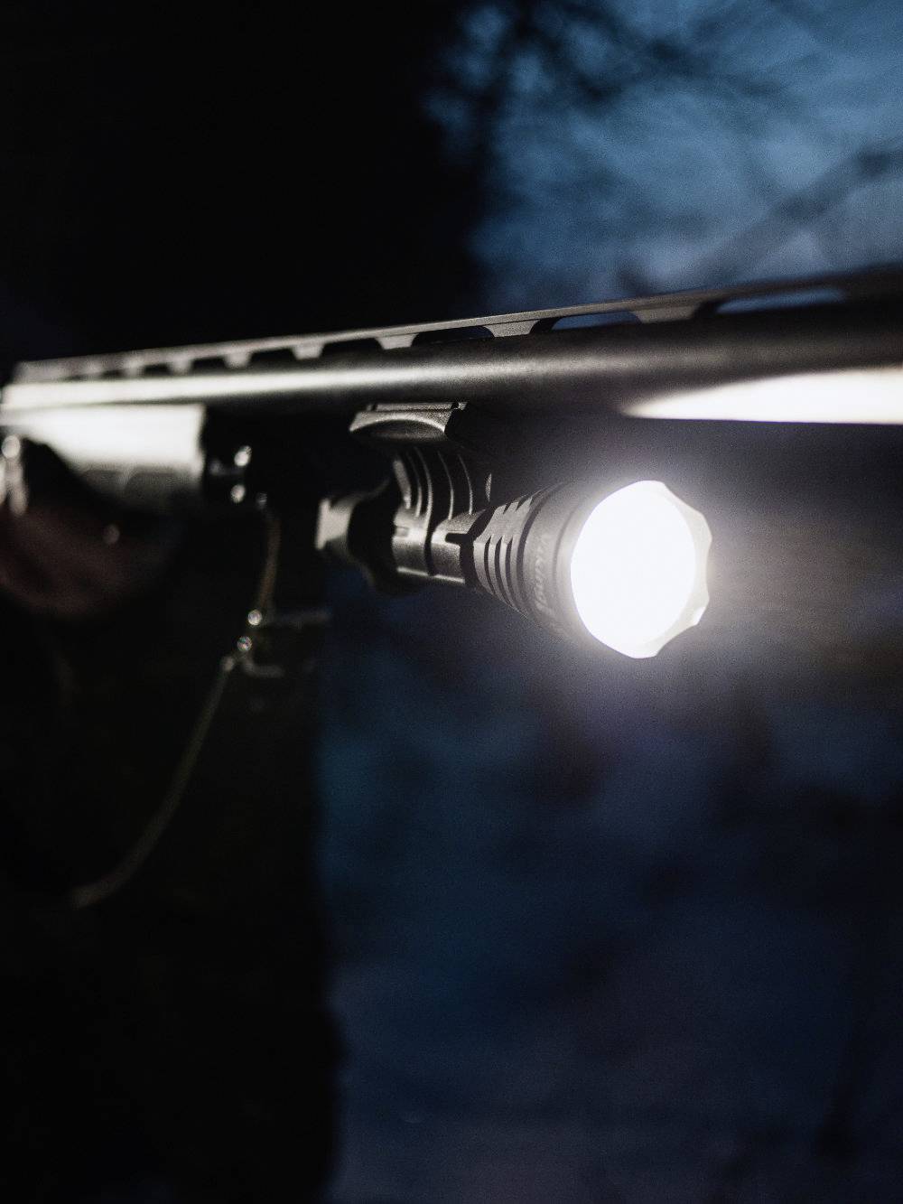 Ein Gewehr mit einer angebrachten Taschenlampe, die in einer dunklen Umgebung leuchtet.