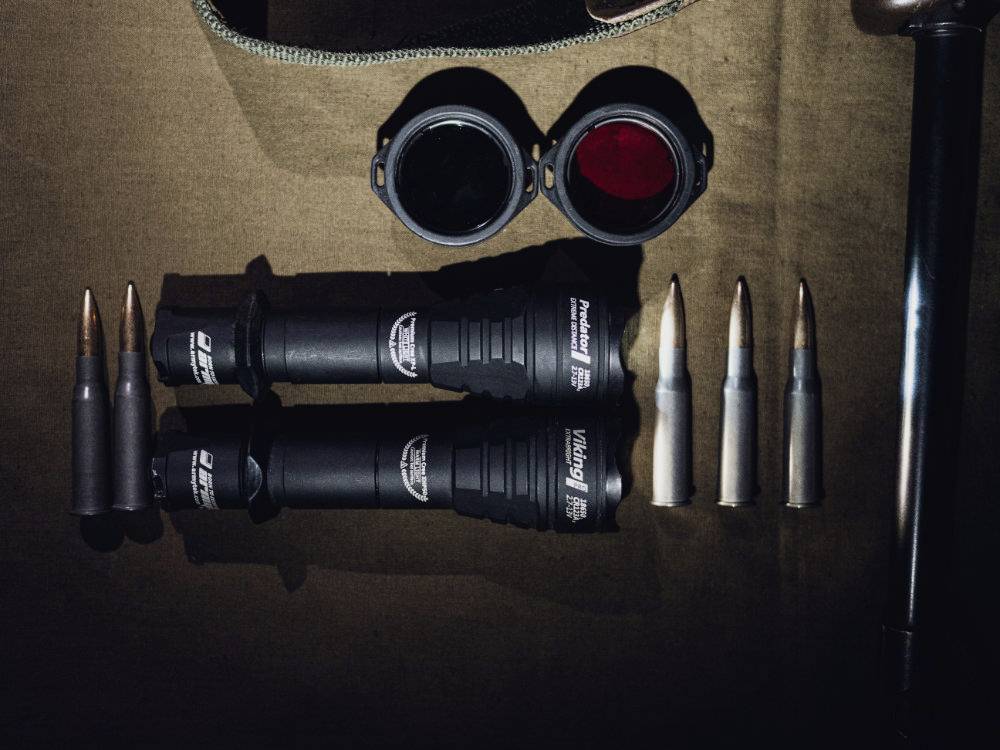 Zwei taktische Taschenlampen und sechs Patronen (teils ungenutzt) liegen auf einem braunen Tuch. Zwei Linsenabdeckungen sind geöffnet.