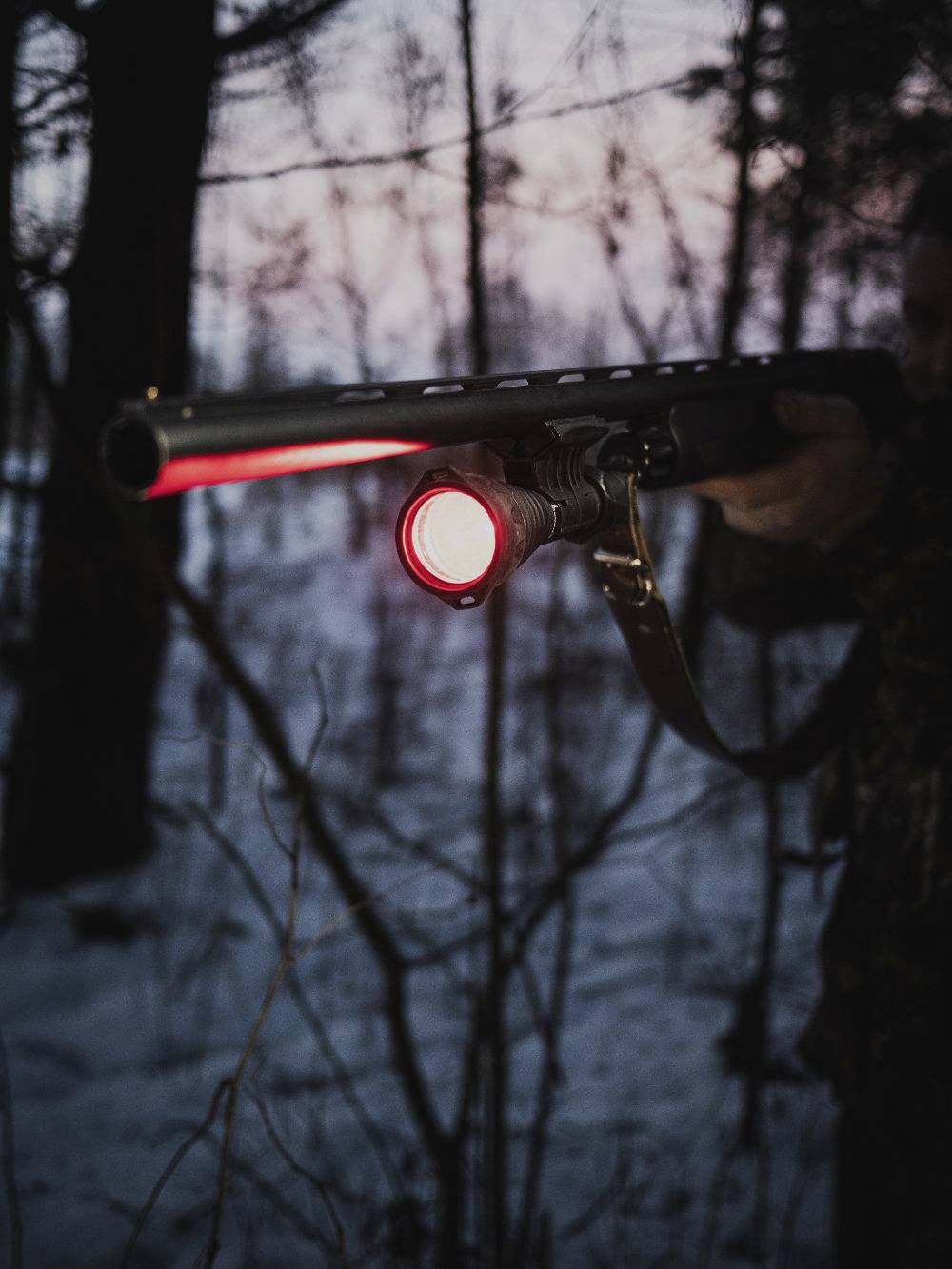 Eine Person im Wald mit einer langen Taschenlampe in der Dämmerung, der rote Lichtstrahl leuchtet in Richtung des Betrachters.