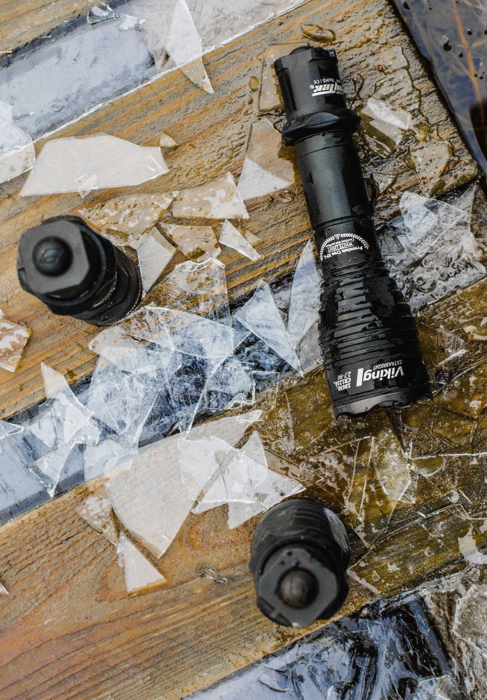 Zerbrochenes Glas liegt auf einem nassen Holzboden, umgeben von robusten Taschenlampen und Flaschen mit matschigen Verschlüssen.