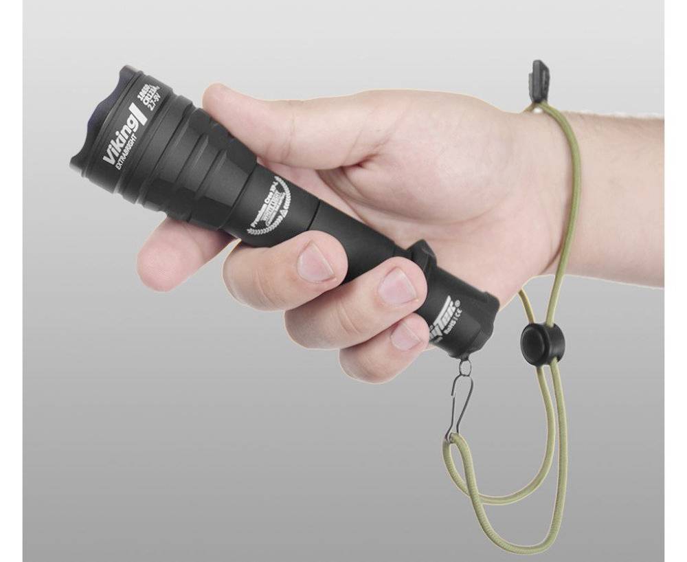 Eine Hand hält eine schwarze Taschenlampe mit einem grünen Handgelenkriemen; die Lampe ist einsatzbereit.