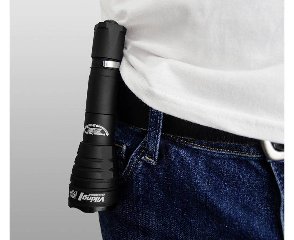 Eine schwarze Taschenlampe ist am Gürtel einer Person in Jeans und weißem Shirt befestigt.