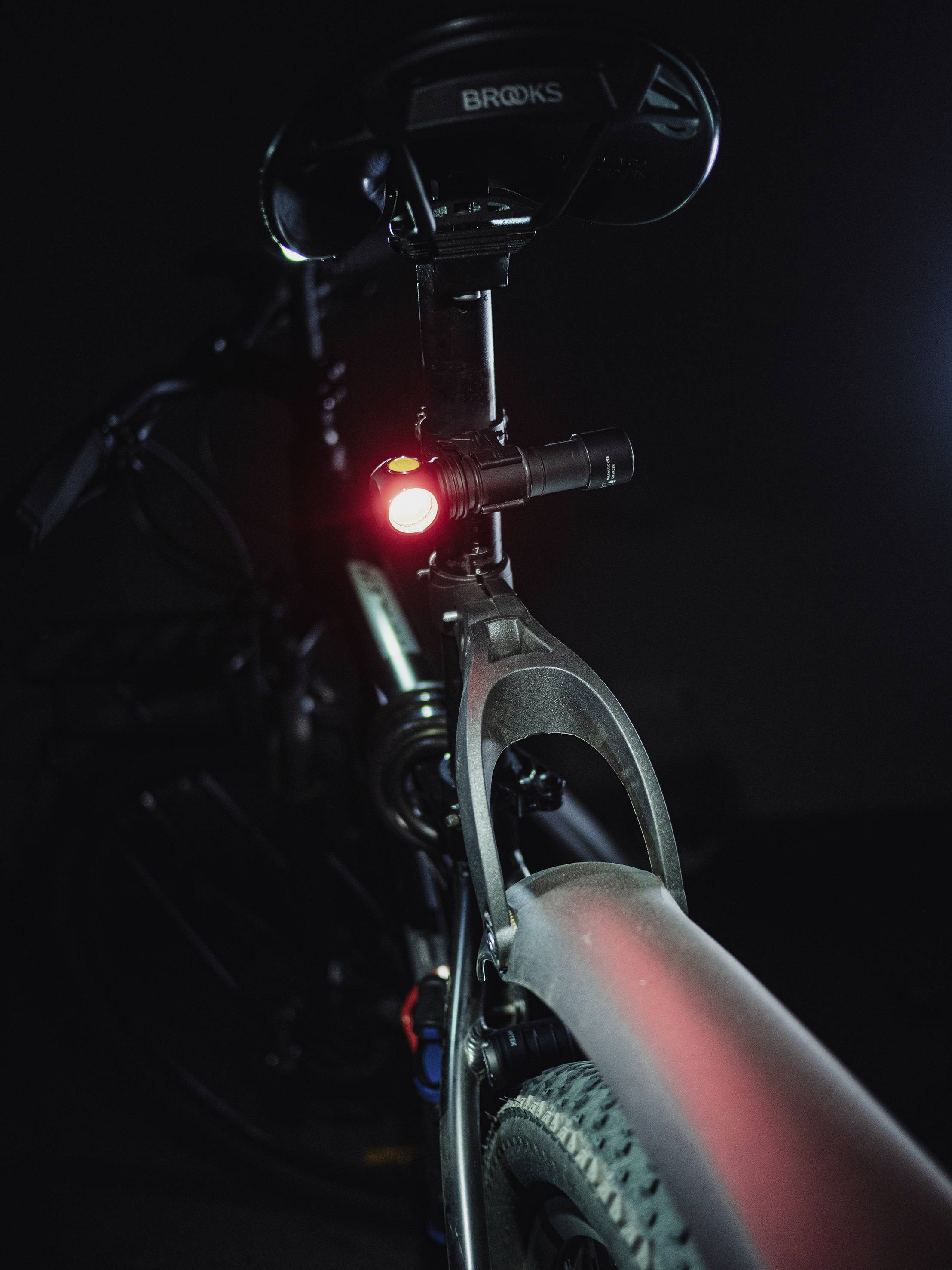 Ein Fahrrad im Dunkeln, beleuchtet von einem roten Rücklicht unter dem Sattel. Der Fokus liegt auf dem Sicherheitsaspekt des Lichts.