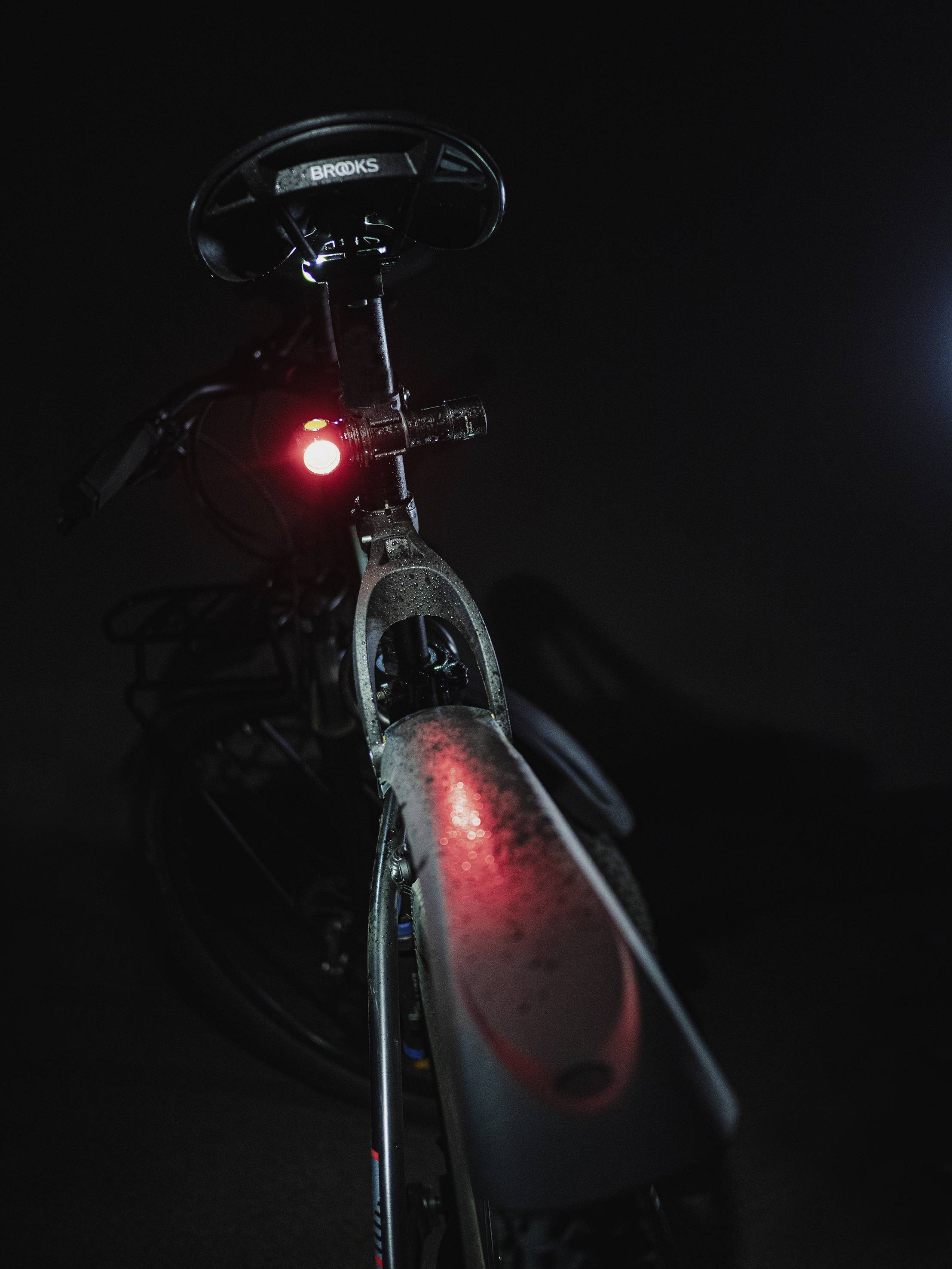Ein Fahrrad von hinten bei schwachem Licht, der Sattel und das rote Rücklicht sind erkennbar. Im Hintergrund ist es dunkel.