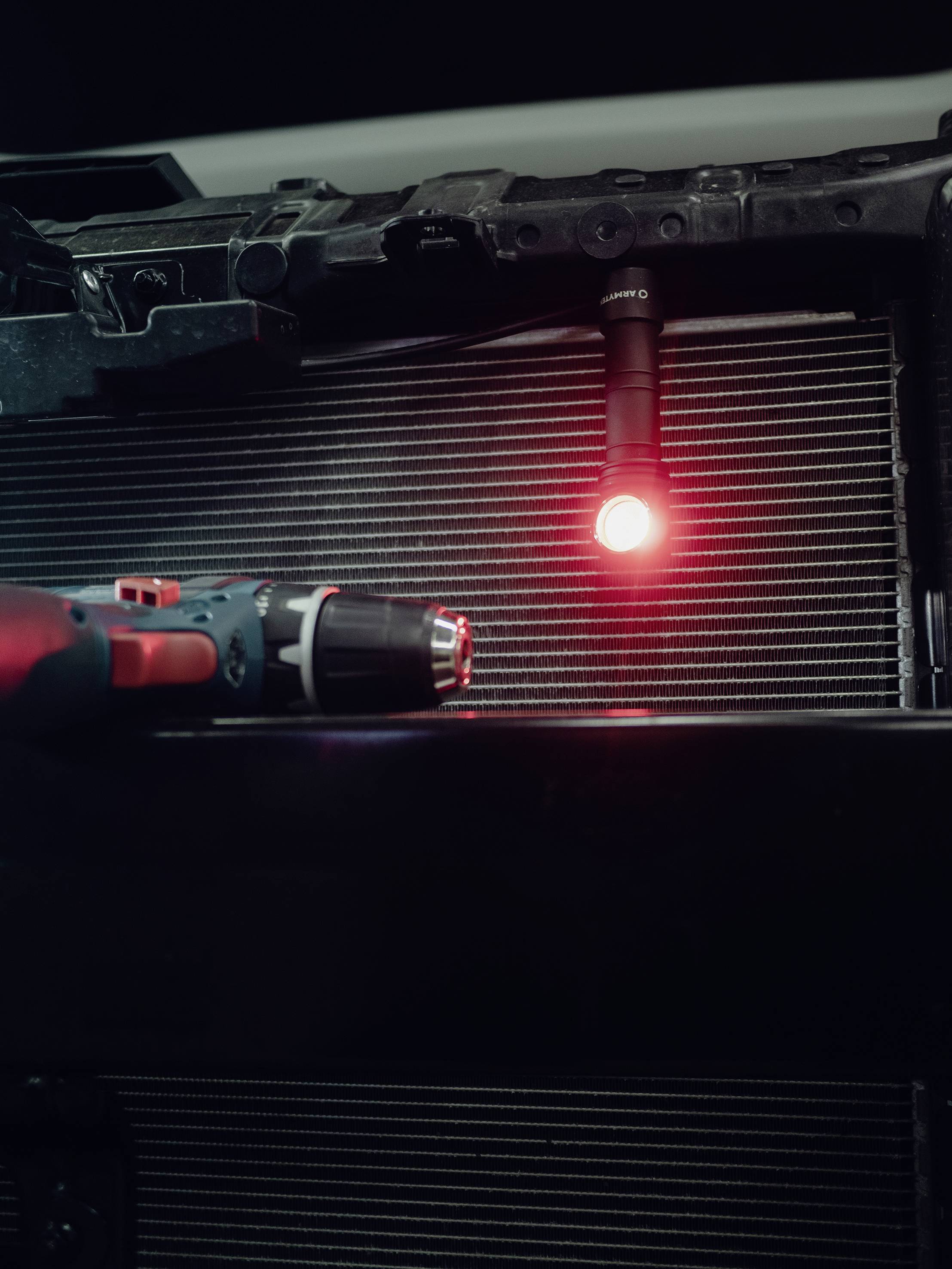 Eine rote LED-Leuchte beleuchtet den Bereich vor einem metallischen Kühlergitter. Im Vordergrund bewegt sich ein Akku-Bohrer.