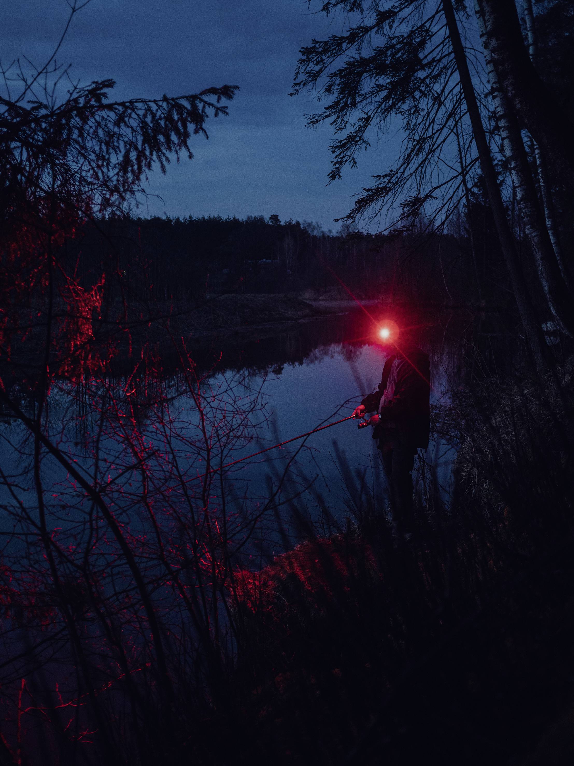 Person angelt bei Nacht am Ufer eines Sees, beleuchtet durch rotes Licht.