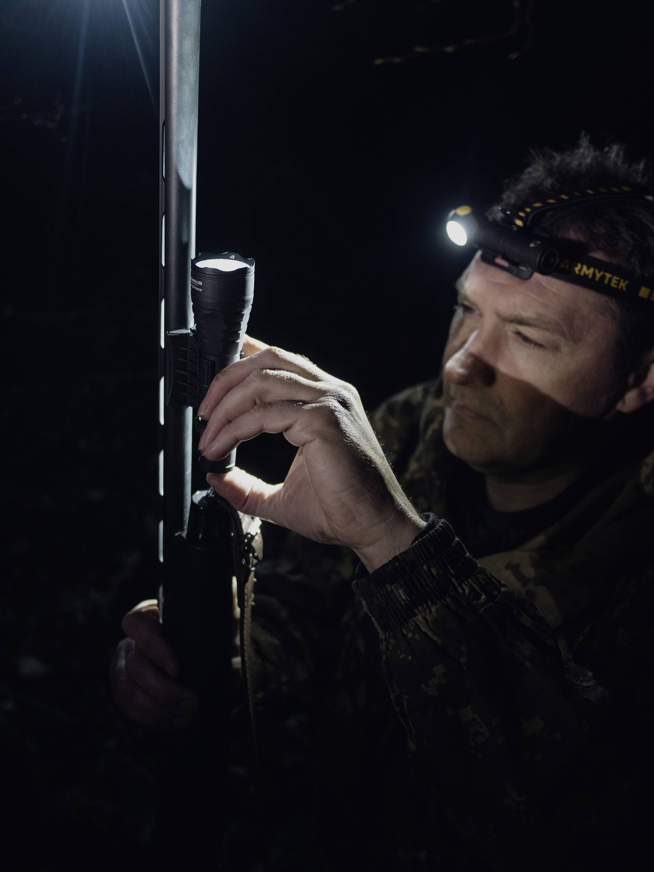 Eine Person mit Stirnlampe hält und untersucht in einem dunklen Umfeld ein Gewehr oder ähnliches Objekt.