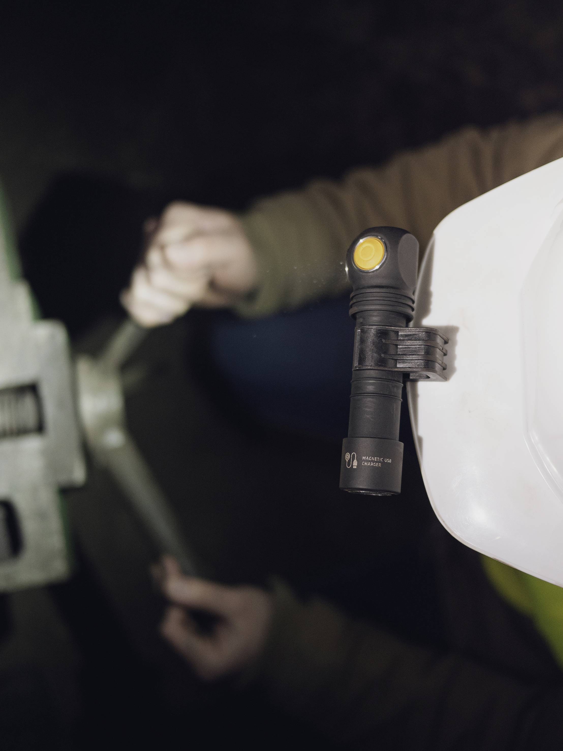 Eine Person trägt einen weißen Schutzhelm mit einer angebrachten Taschenlampe und arbeitet mit einem Schraubenschlüssel an einer Maschine.