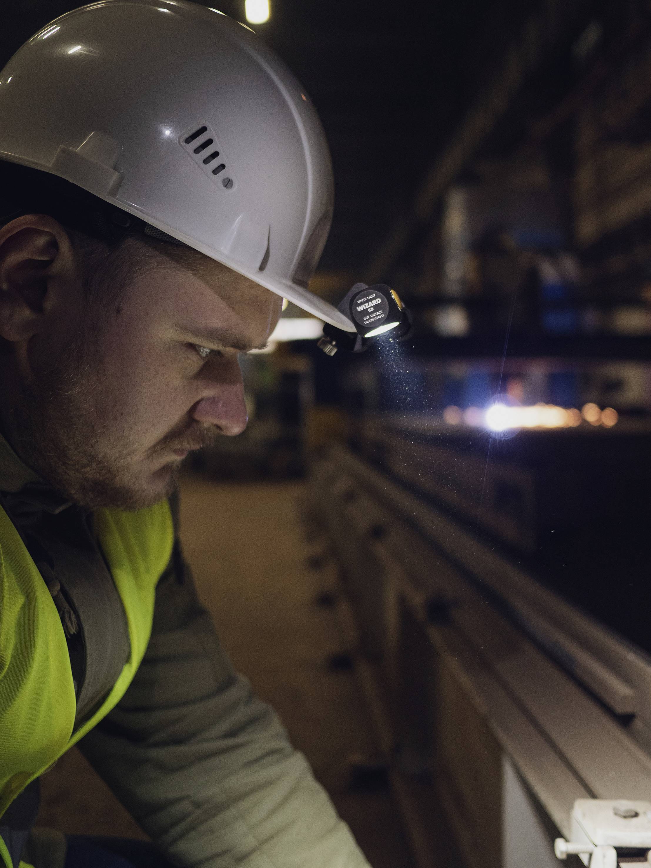 Ein Mann mit Schutzhelm und Warnweste inspiziert konzentriert eine Maschine in einer Fabrikhalle.