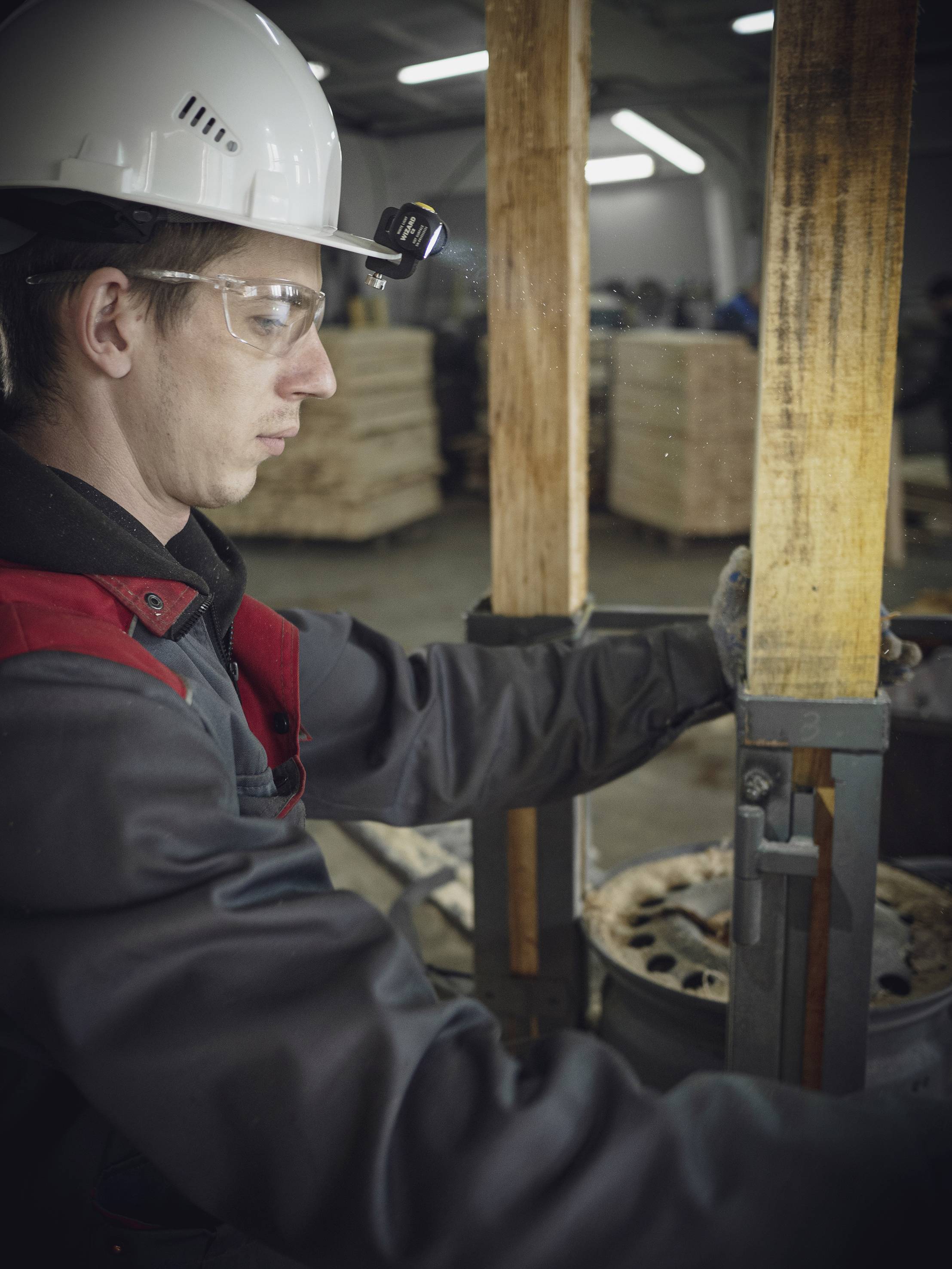 Ein Arbeiter in Schutzkleidung bedient eine Maschine in einer Fabrikhalle. Im Hintergrund sind Holzpaletten zu sehen.